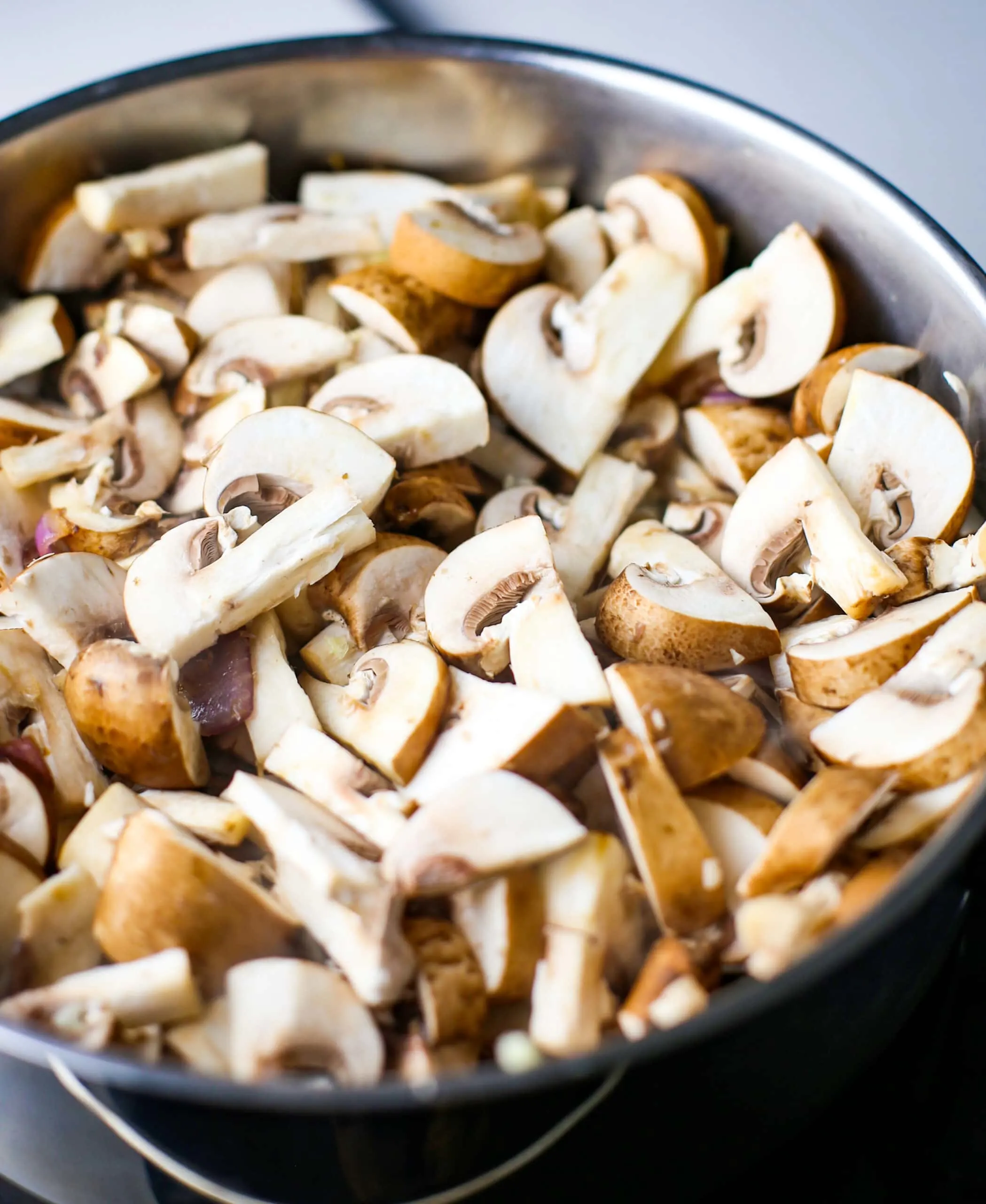 Sliced cremini mushrooms in a stainless steel saucepan.