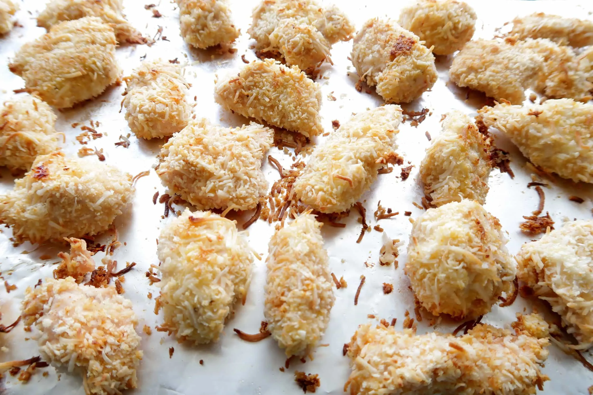 Baked crispy coconut chicken nuggets bites on an aluminum foil lined baking sheet.