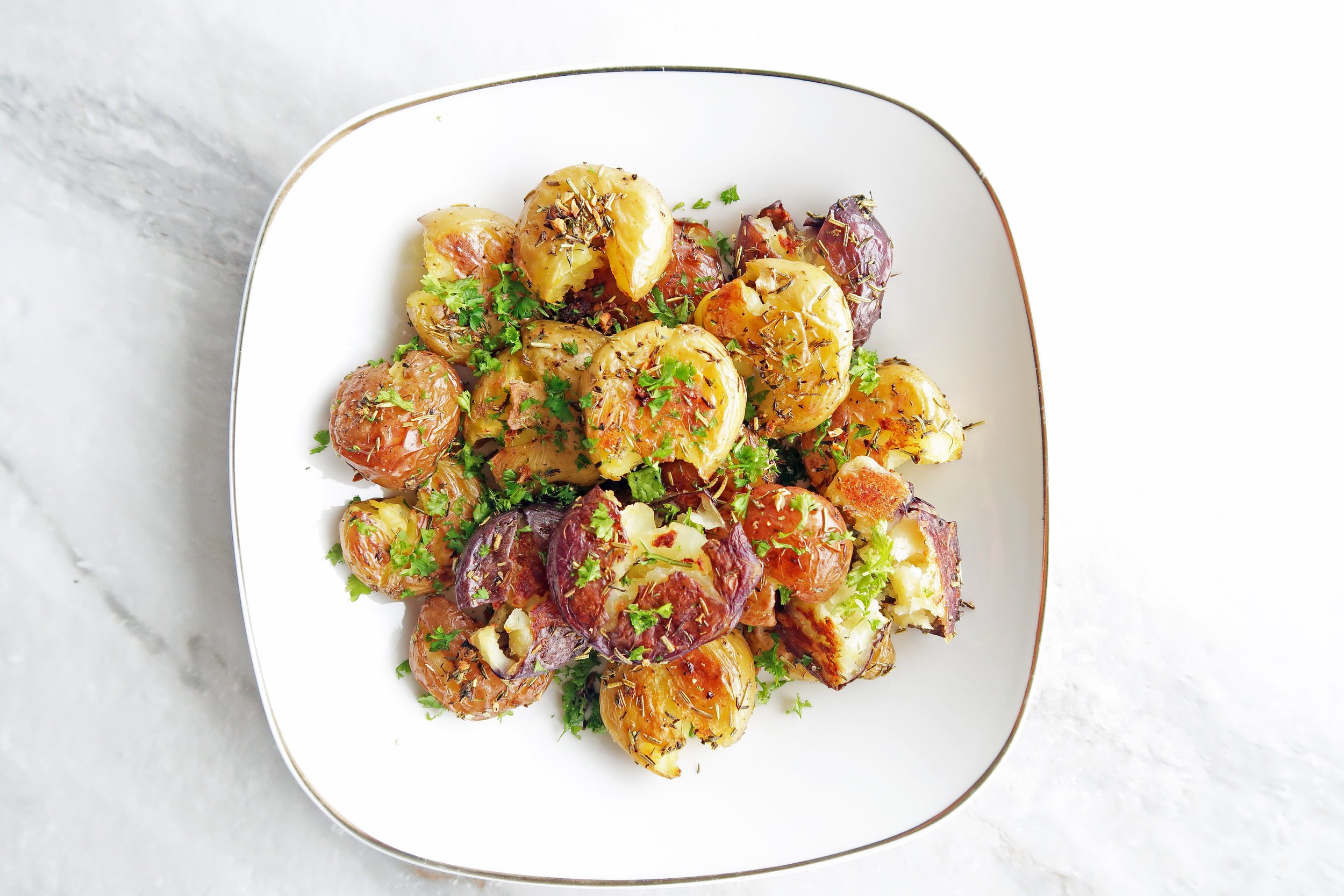 Crispy Garlic Smashed Baby Potatoes on a white plate; An easy, gluten-free, vegan side dish with a crispy outside and fluffy inside.