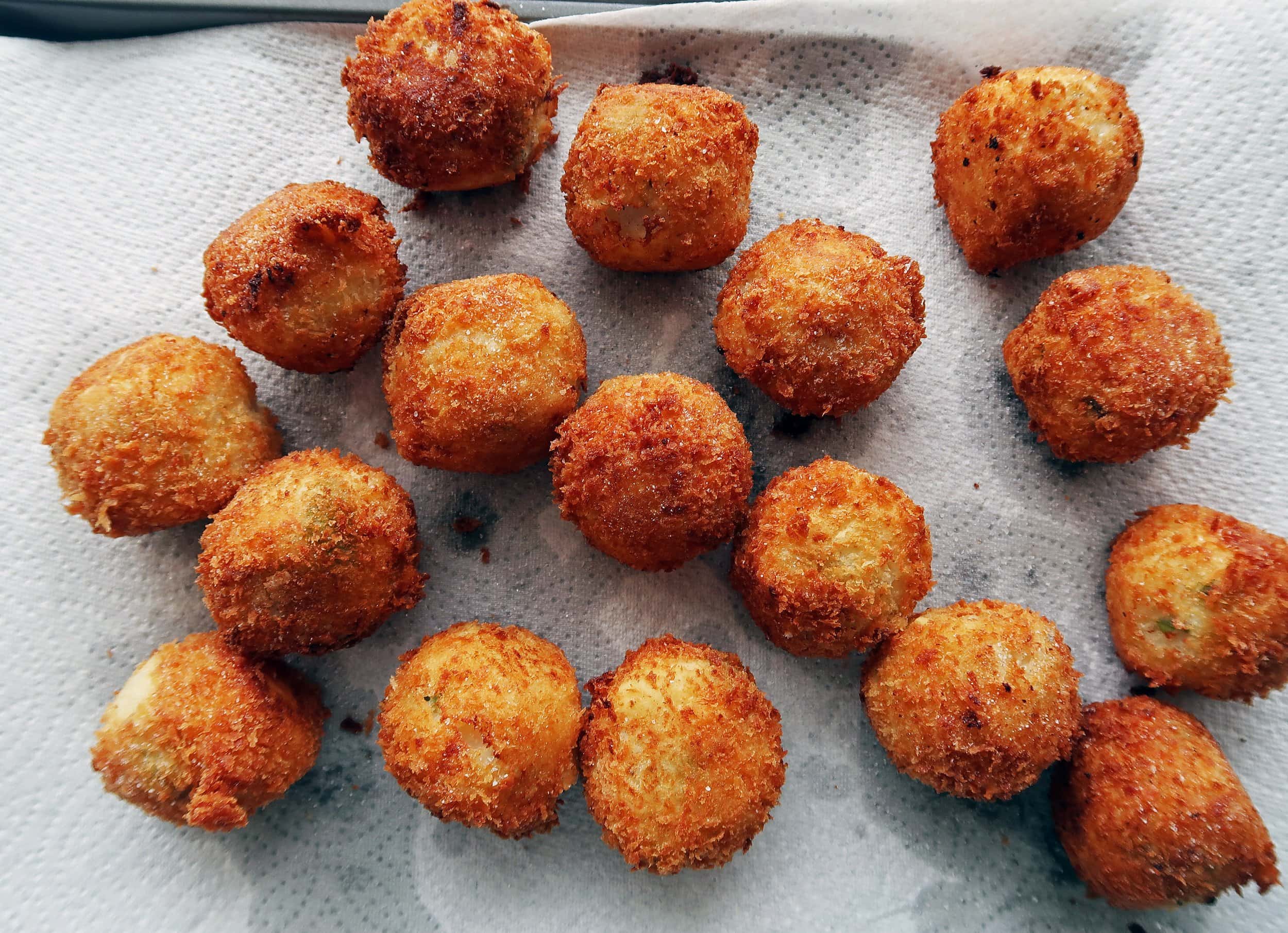 Crispy mashed potato cheese balls cooling on a paper towel.