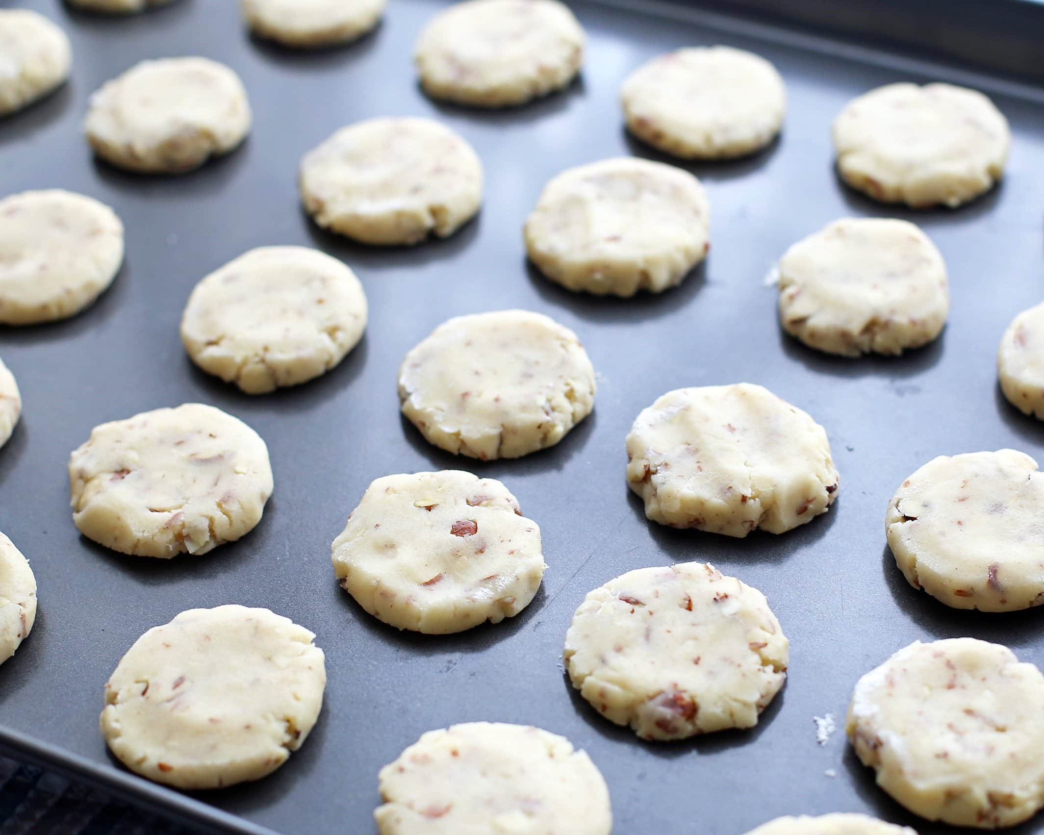 Pre-baked flattened almond cookie dough balls on a baking sheet.