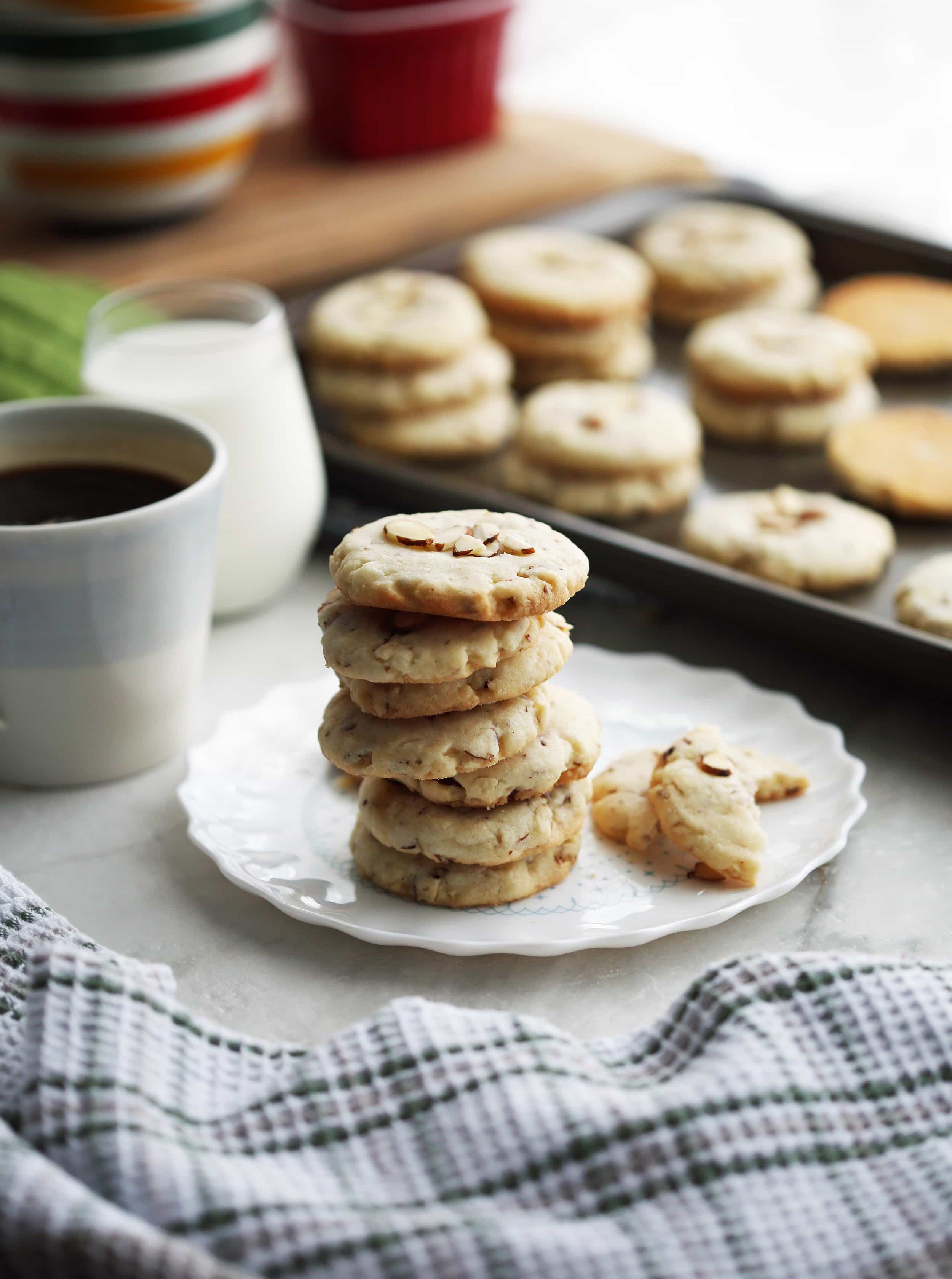 Side view of stacked crunchy almond cookies with more cookies on a baking sheet in the background.