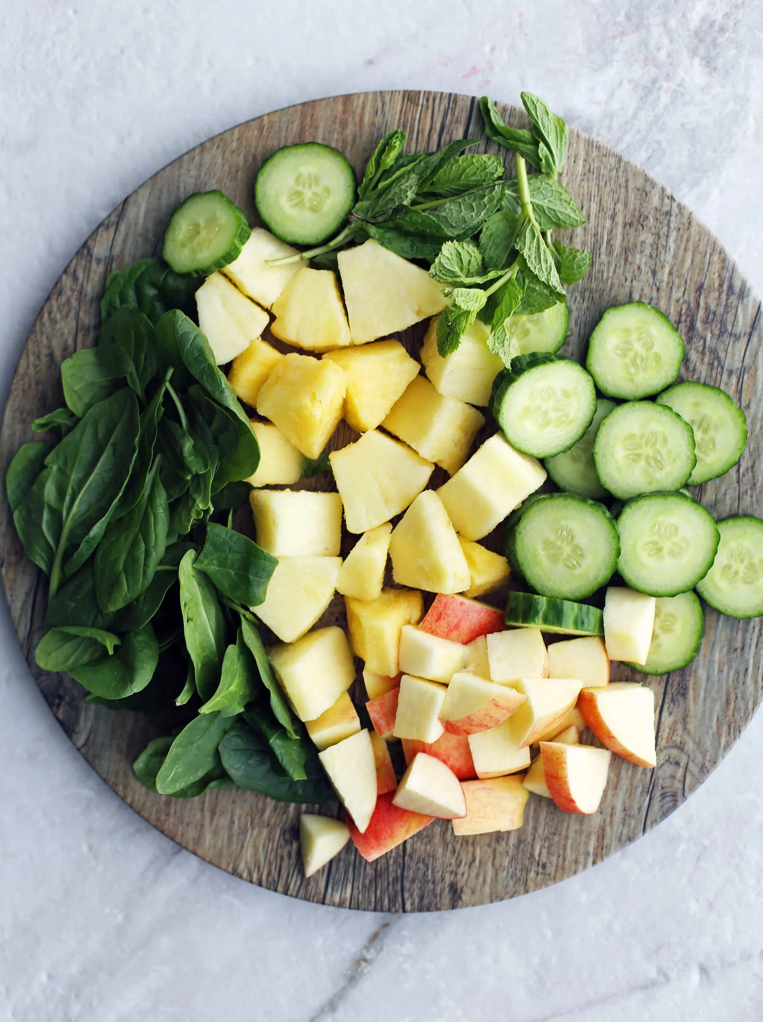 A large wooden platter contained chopped pineapples, apples, cucumber, mint and baby spinach.