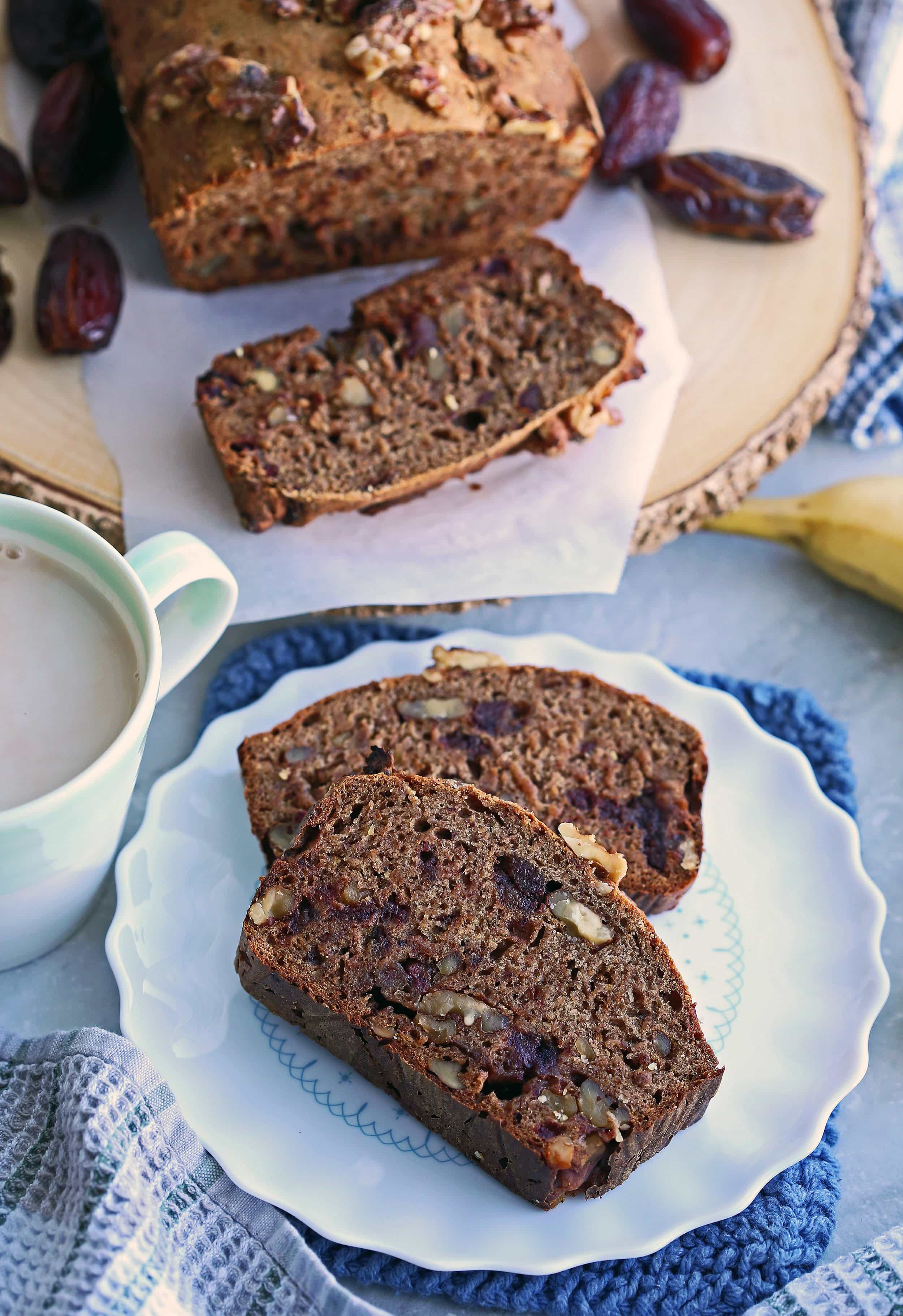 Two slices of Date Banana Nut Bread on a white platter with the rest of the loaf on a wooden platter behind it.
