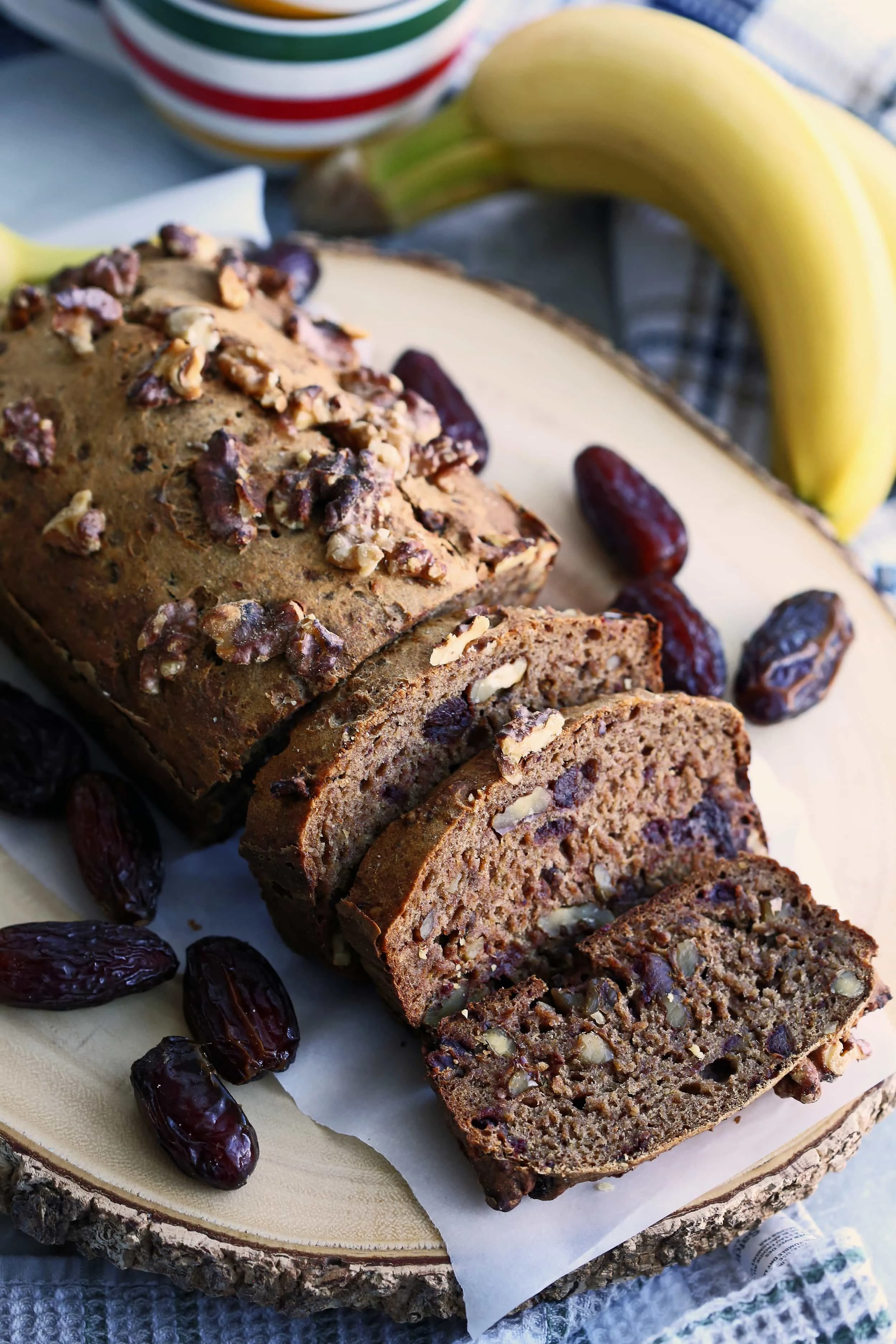 Sliced Date Banana Nut Bread surrounded by Medjool dates on a round wooden platter.