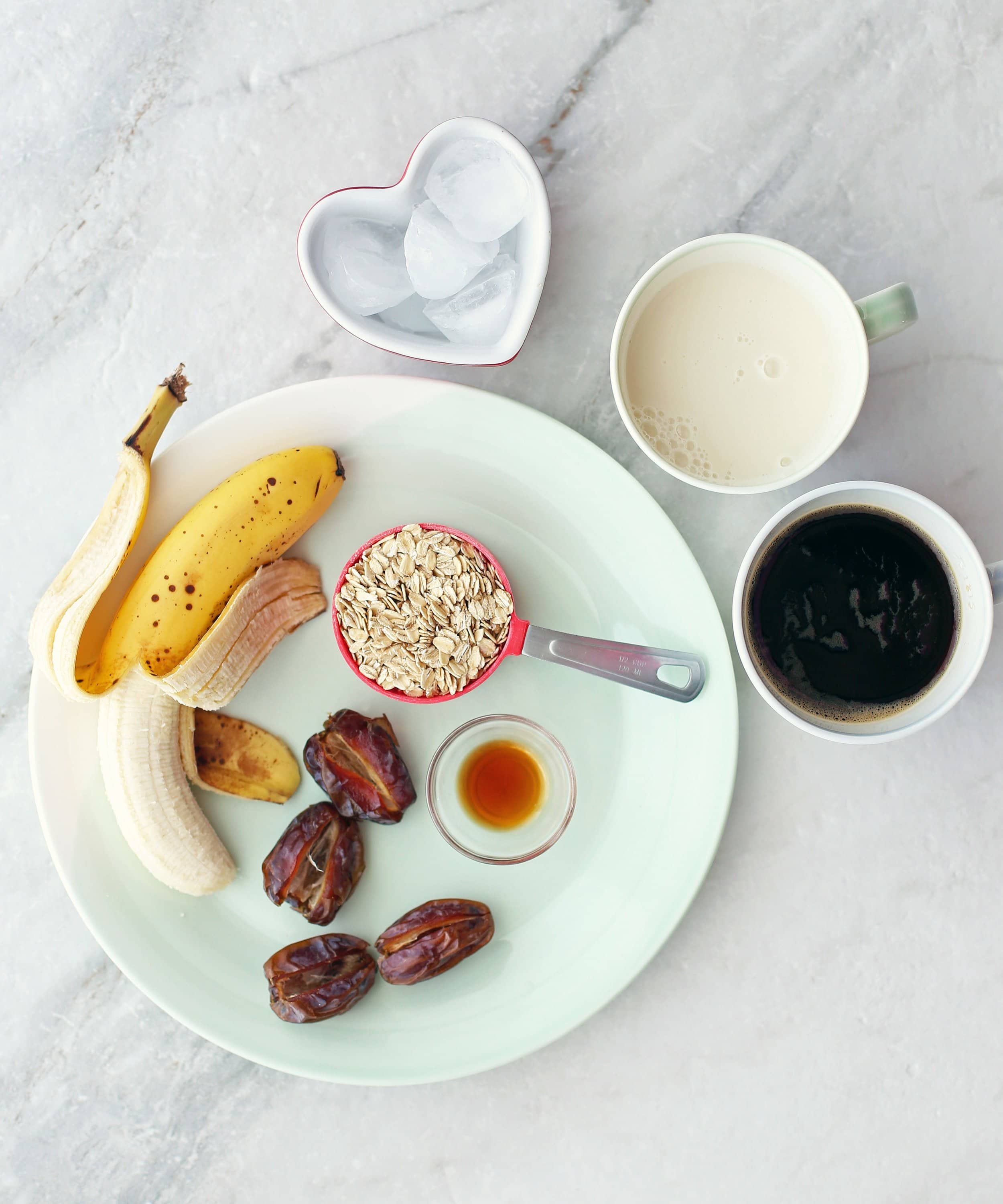 Medjool dates, a banana, rolled oats, vanilla extract, milk, coffee, and ice in bowls and on a plate.