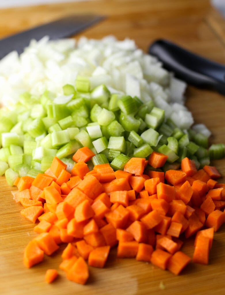 Diced carrots, onions, and celery on a cutting board.