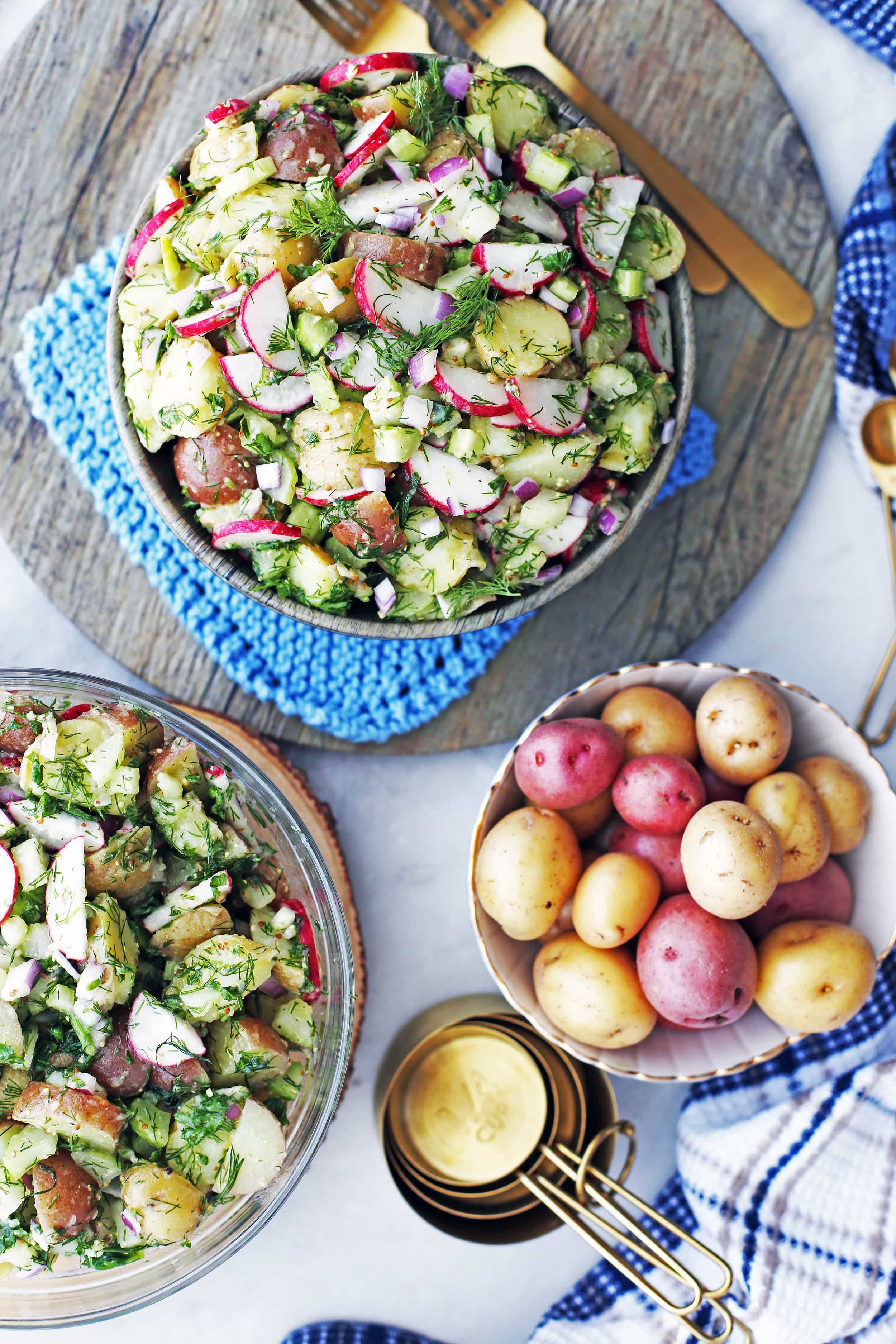 Overhead view of a wooden bowl and large glass bowl of Mustard Dill Potato Salad and another bowl of baby potatoes.