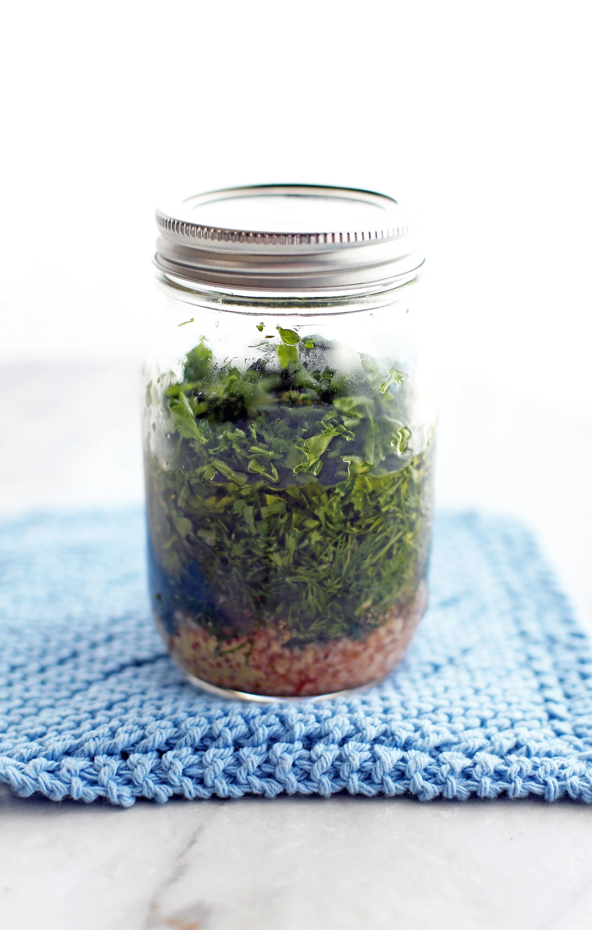 A mason jar full of unshaken olive oil, red wine vinegar, dill, parsley. garlic,dijon mustard, salt, and pepper.