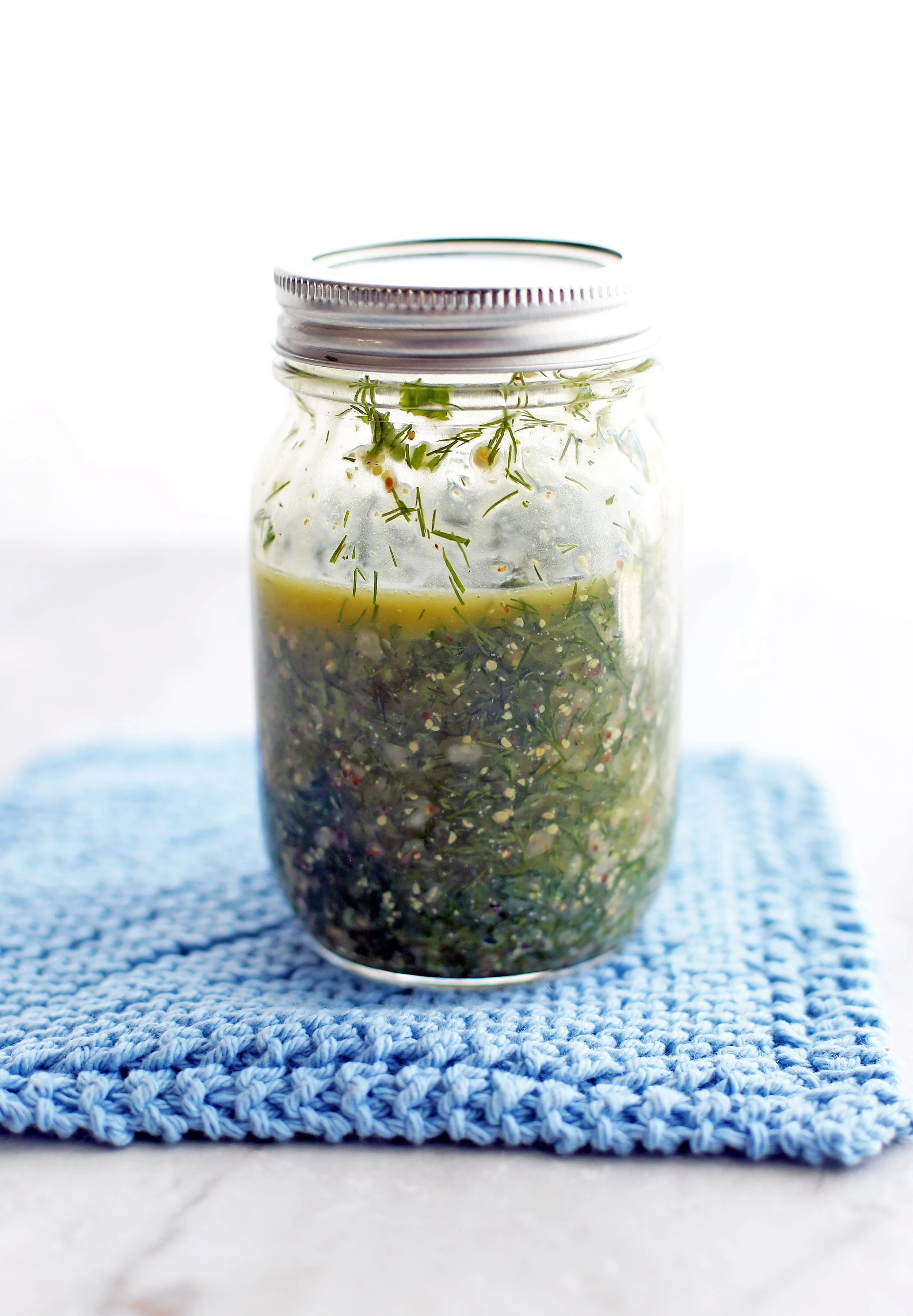 A mason jar containing olive oil, red wine vinegar, dill, parsley. garlic,dijon mustard, salt, and pepper shaken together to form a vinaigrette.