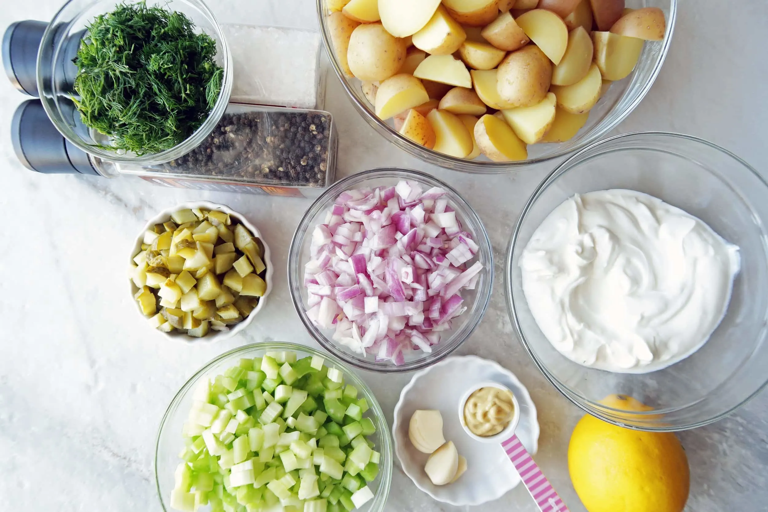 Separate bowls of potatoes, dill, onions,celery, red onions, and Greek yogurt.