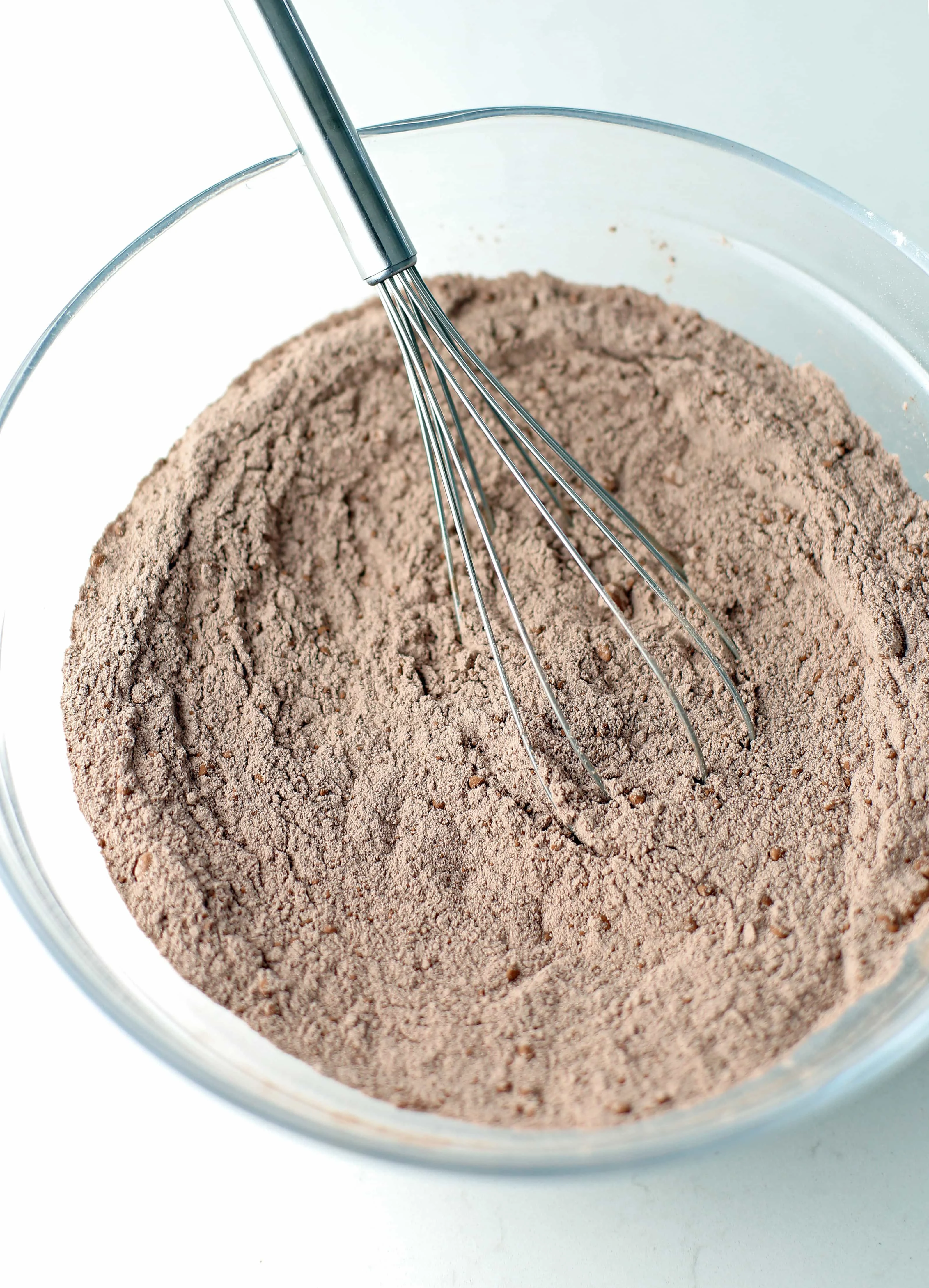 Dry baking ingredients including cocoa power and all-purpose flour mixed in a glass bowl.