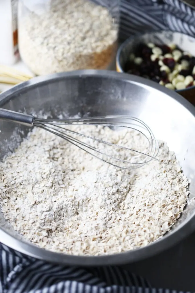 Dry ingredients for oatmeal cookies in a stainless steel bowl with a wired whisk in it.