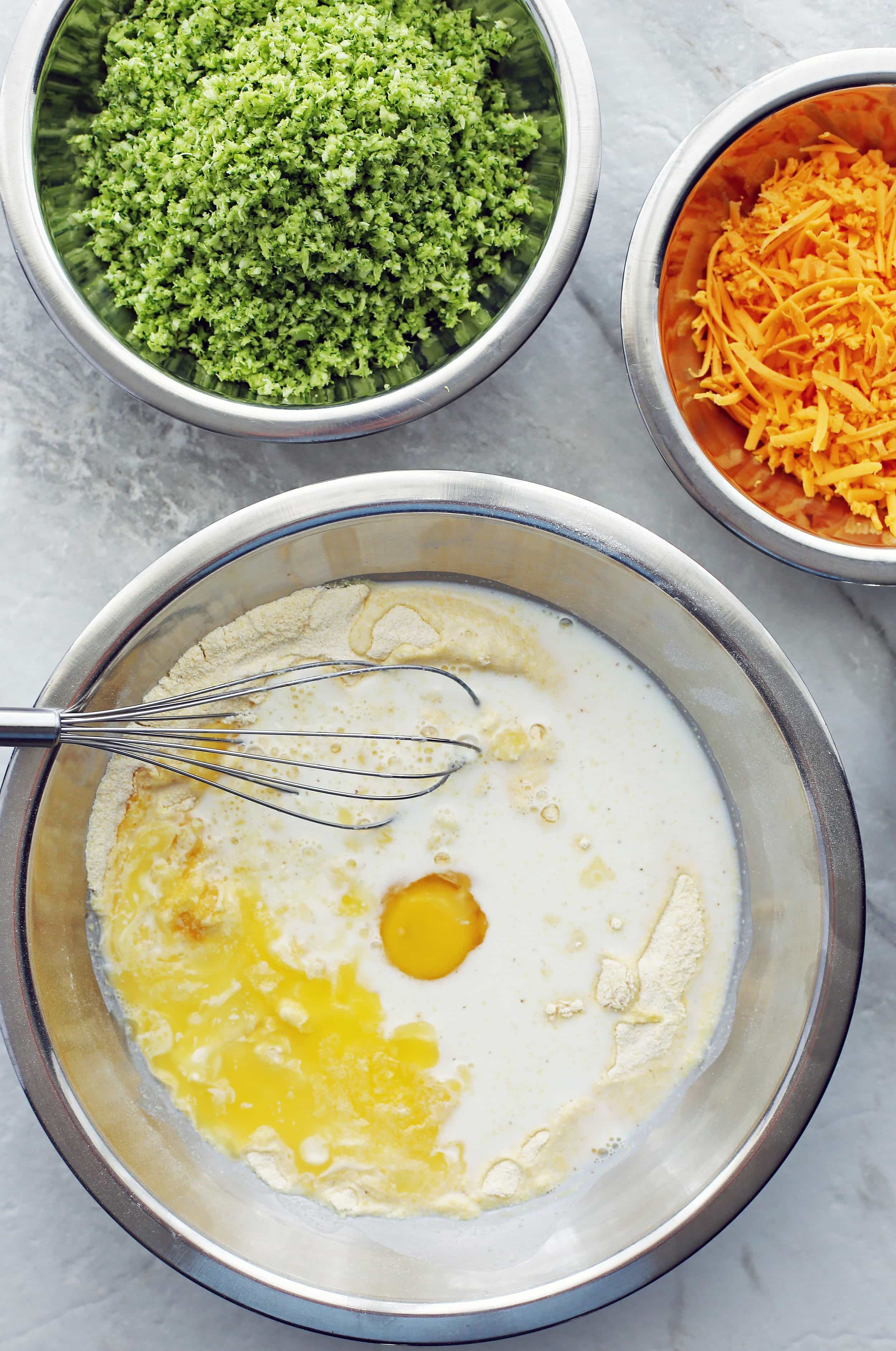 A metal bowl containing milk. melted butter, and an egg.