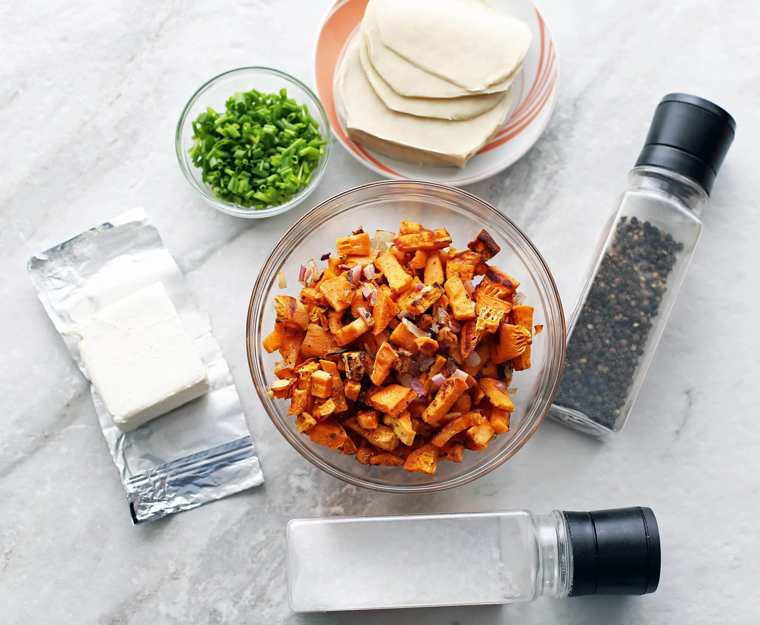 Overhead view of roasted butternut squash, dumpling wrappers, cream cheese, and green onions.