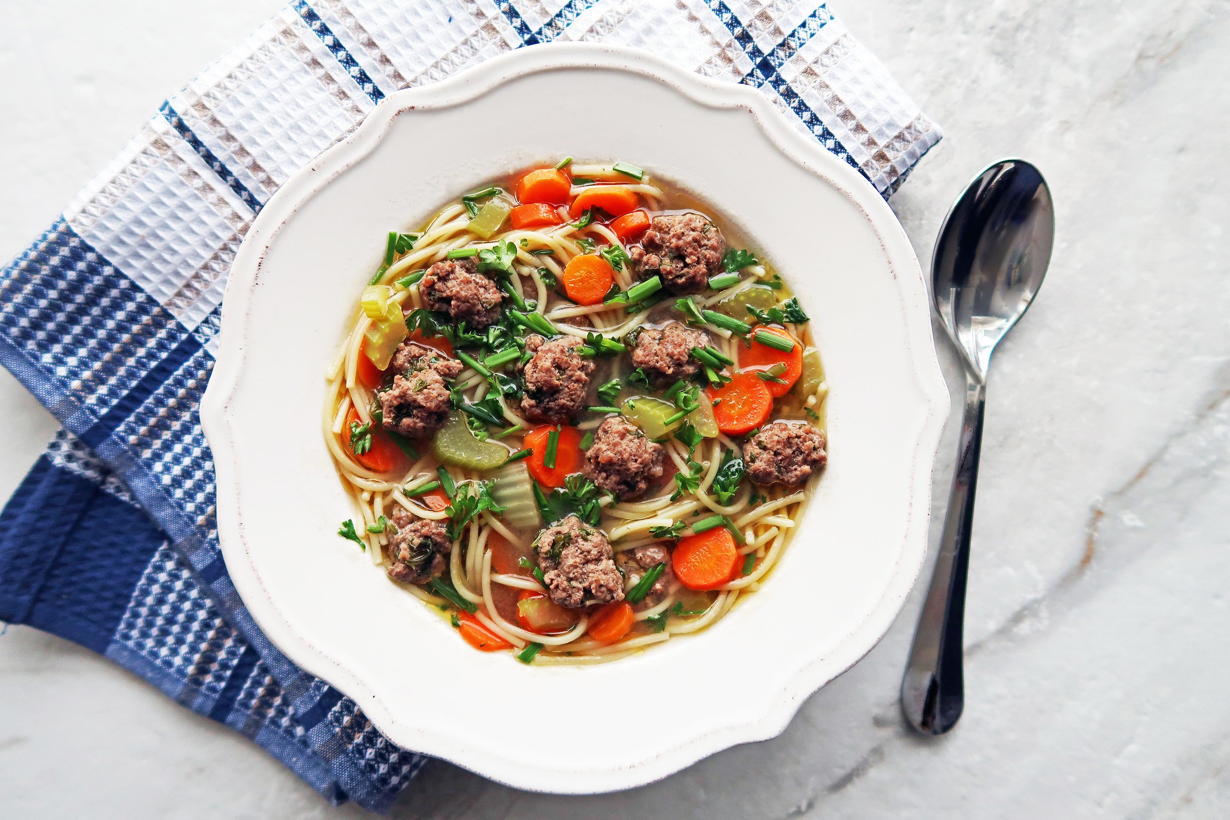 A bowl of Dutch Vegetable Soup with Meatballs next to a spoon.