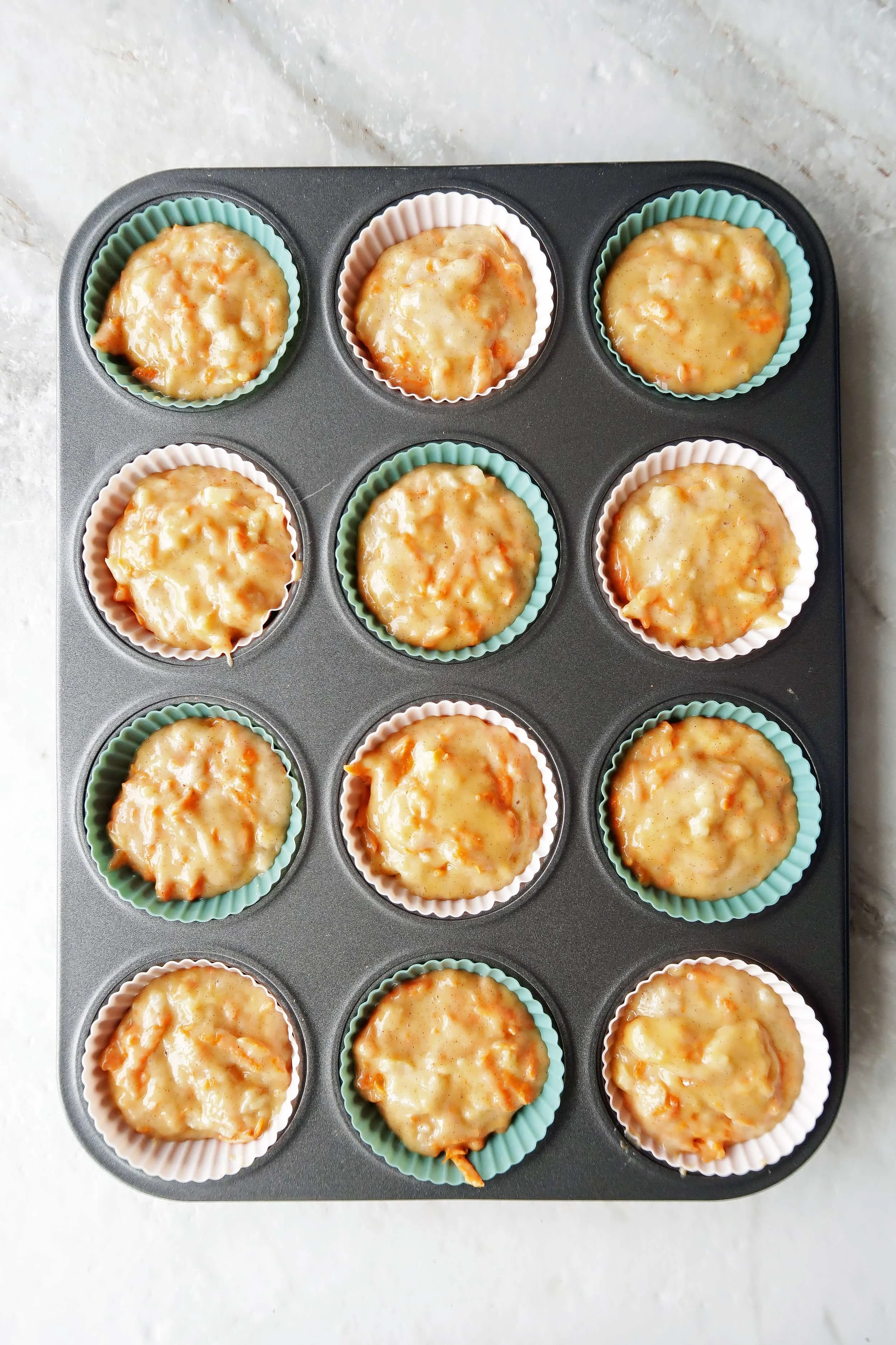 Pineapple carrot muffin batter placed in a dozen silicone liners in a muffin tin.