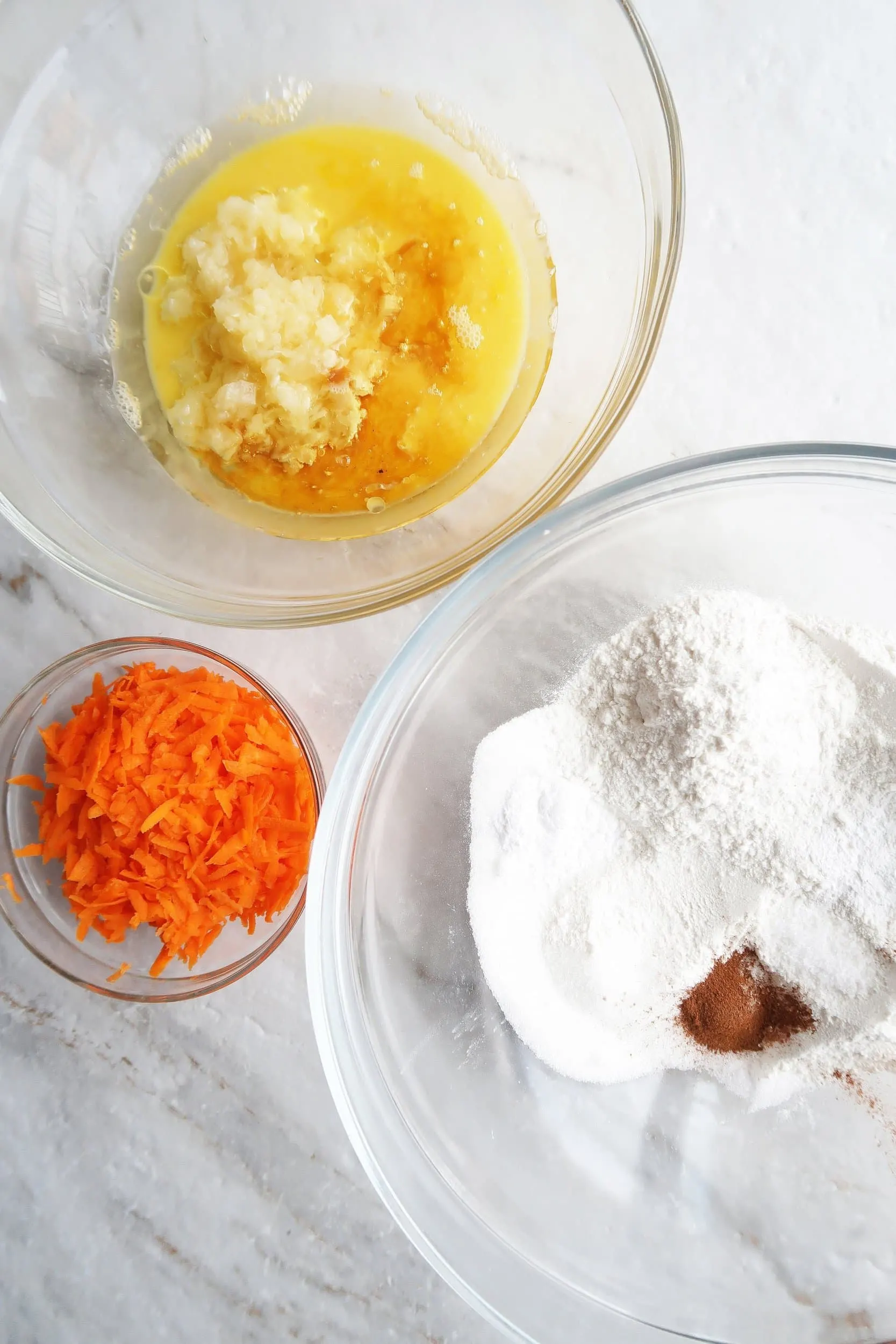 Bowls of shredded carrots and wet and dry muffin ingredients, including crushed pineapple and vegetable oil.