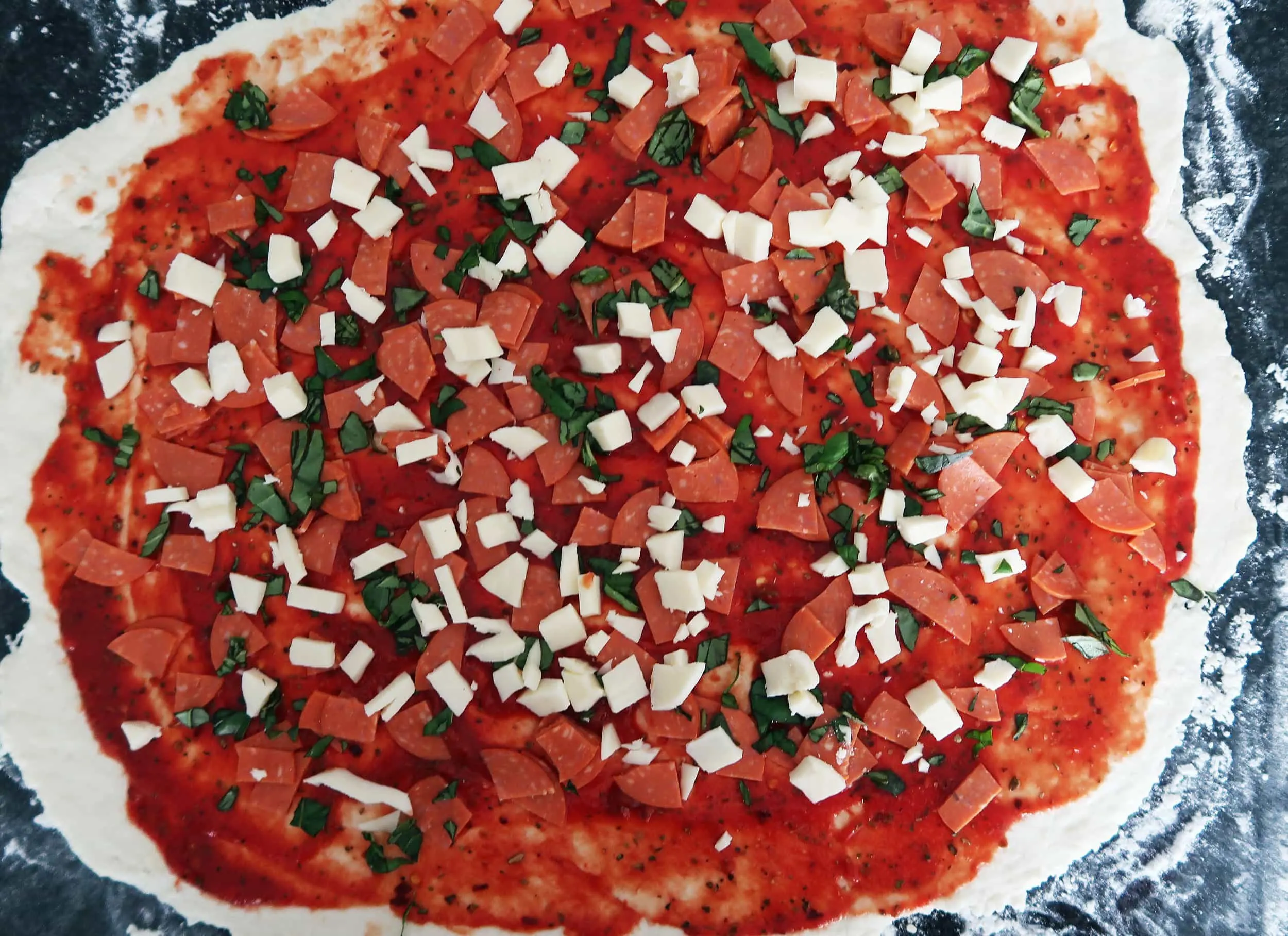 Pizza dough topped with tomato sauce, pepperoni, cheese, and basil.