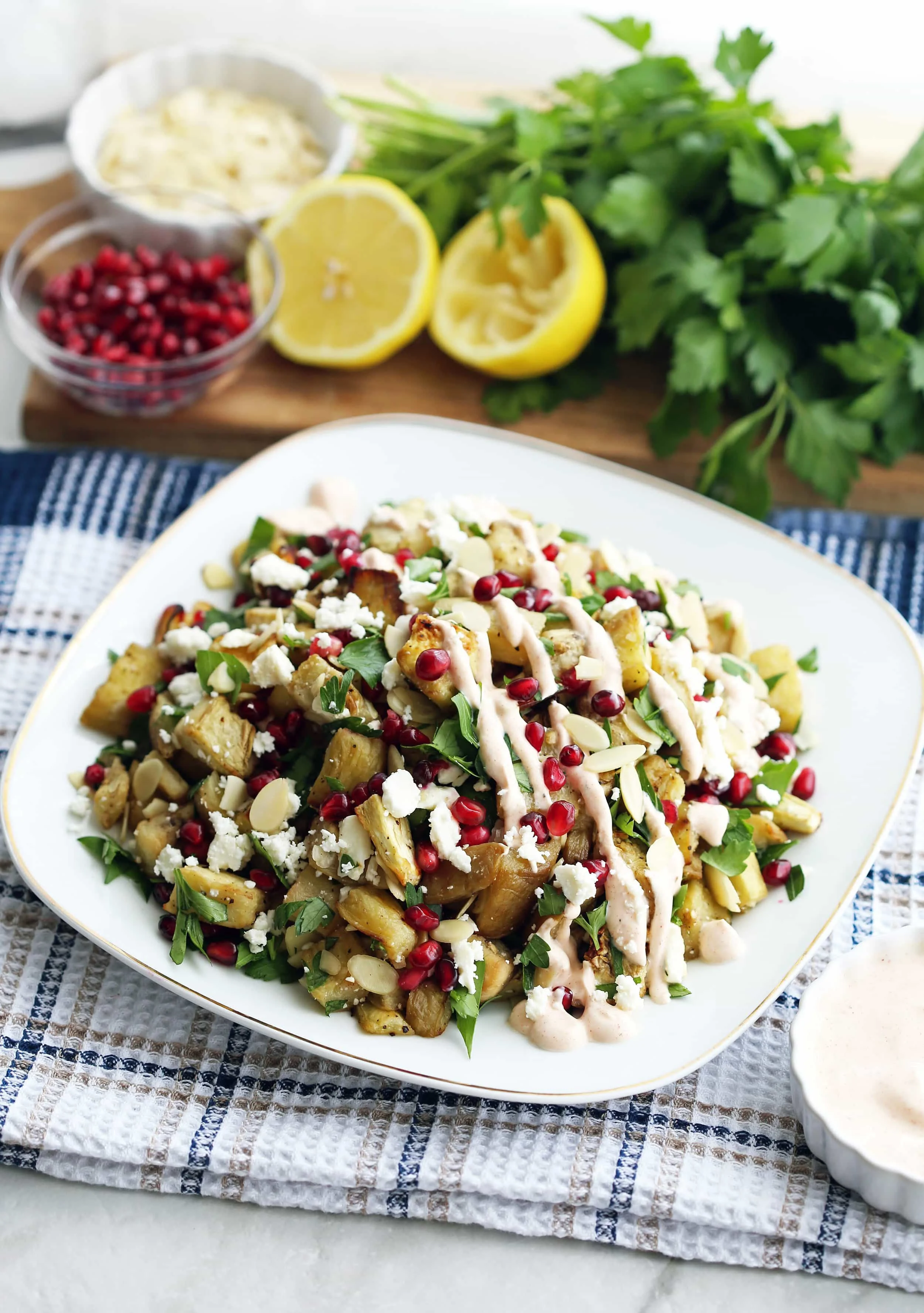 A white plate full of roasted eggplant pomegranate feta salad with smoked paprika yogurt dressing drizzled on top.