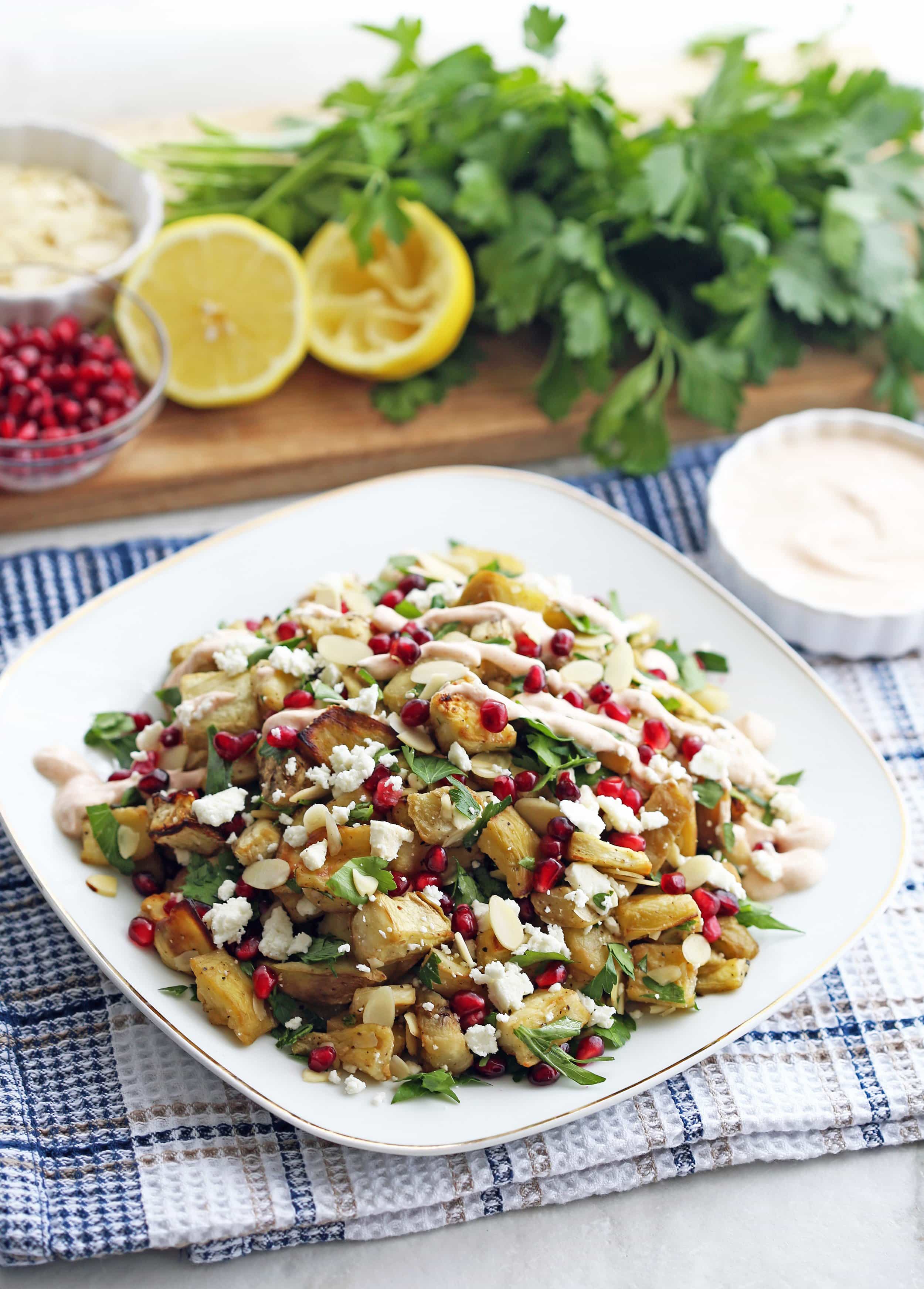 A white plate full of roasted eggplant pomegranate feta salad with smoked paprika yogurt dressing drizzled on top.
