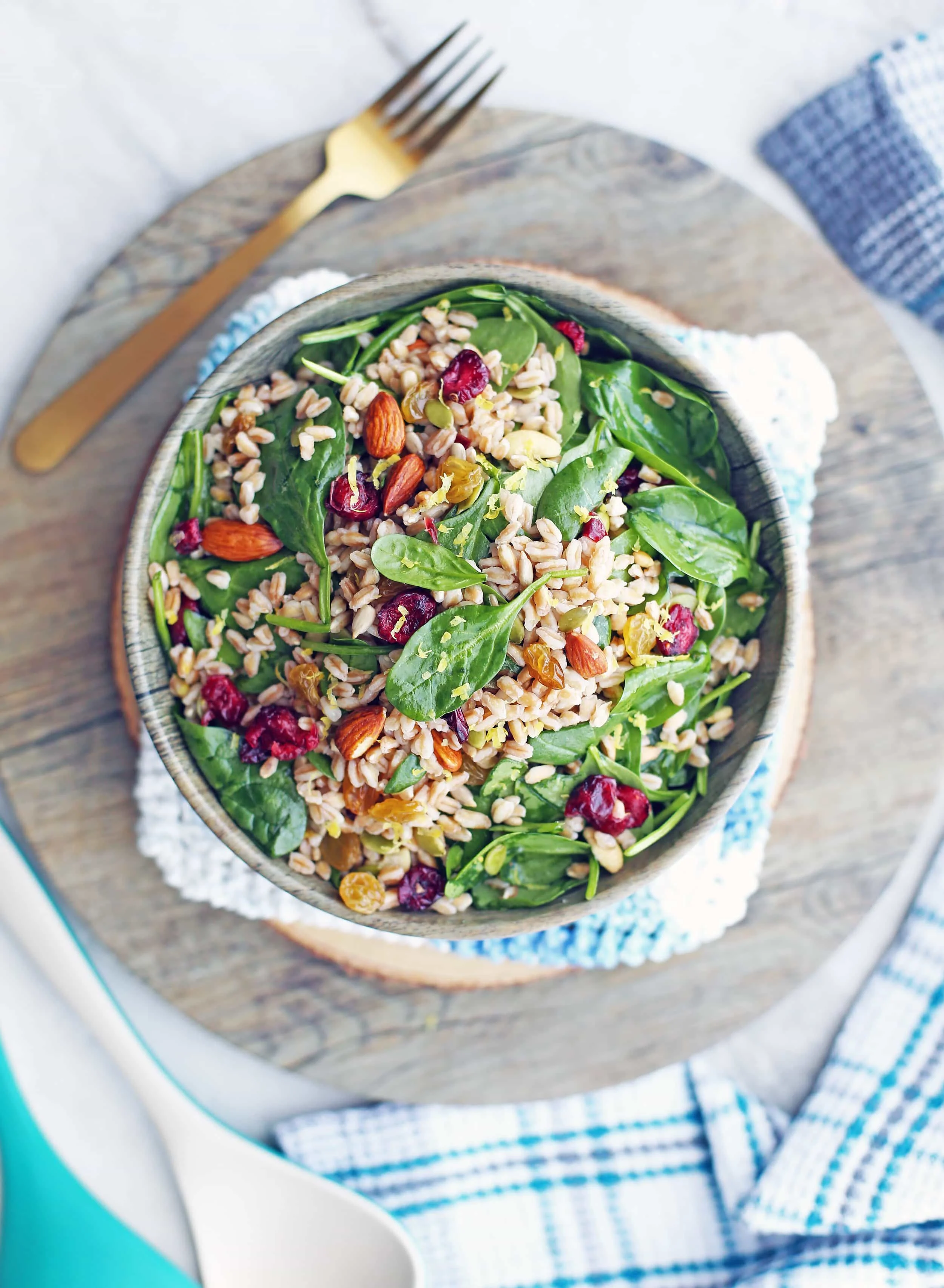 Overhead view of a salad containing farro, baby spinach, dried fruit, nuts, and seeds in a wooden bowl.