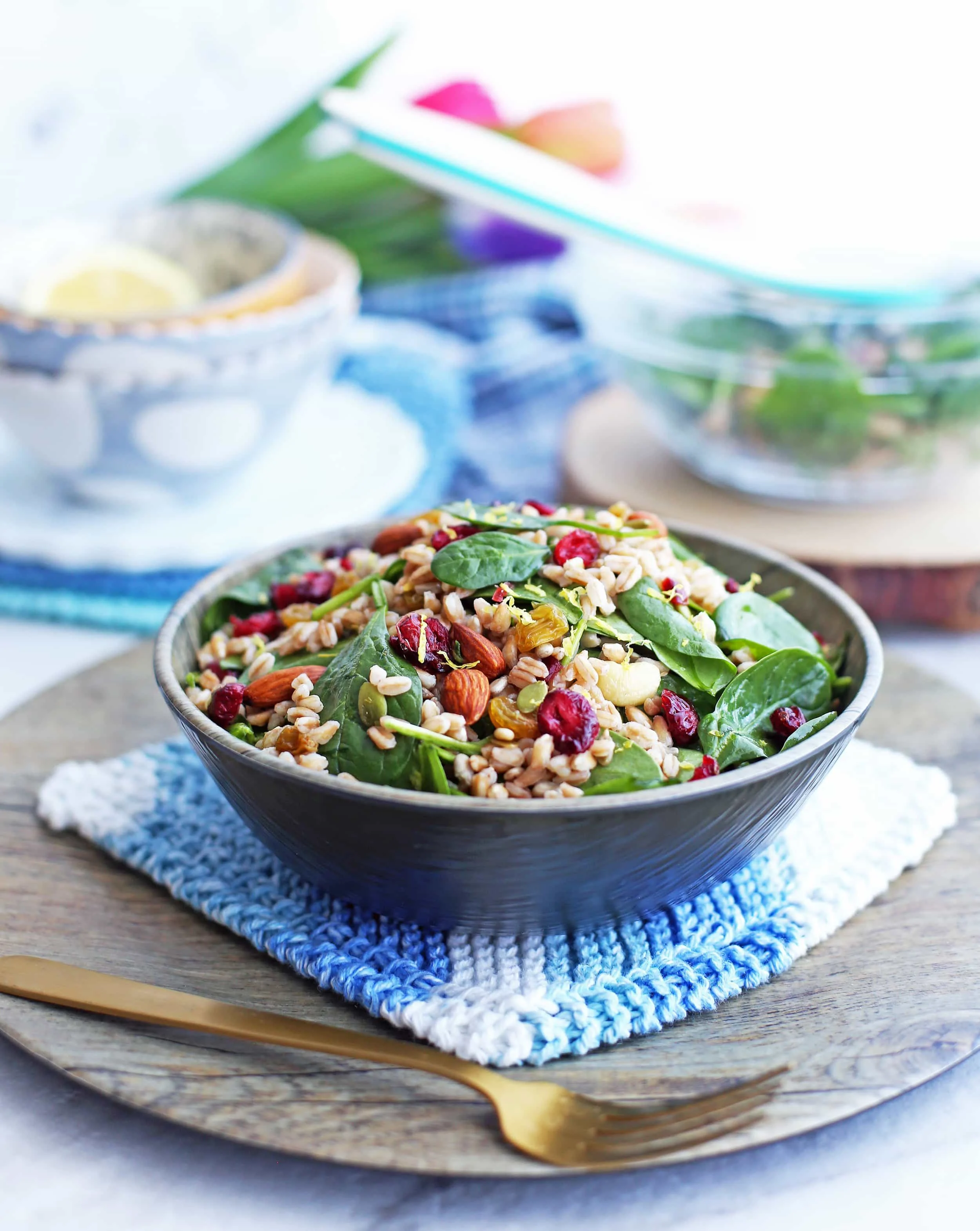 Farro and Spinach Salad with Dried Fruit and Nuts in a wooden bowl with a fork to its side; more salad behind it.