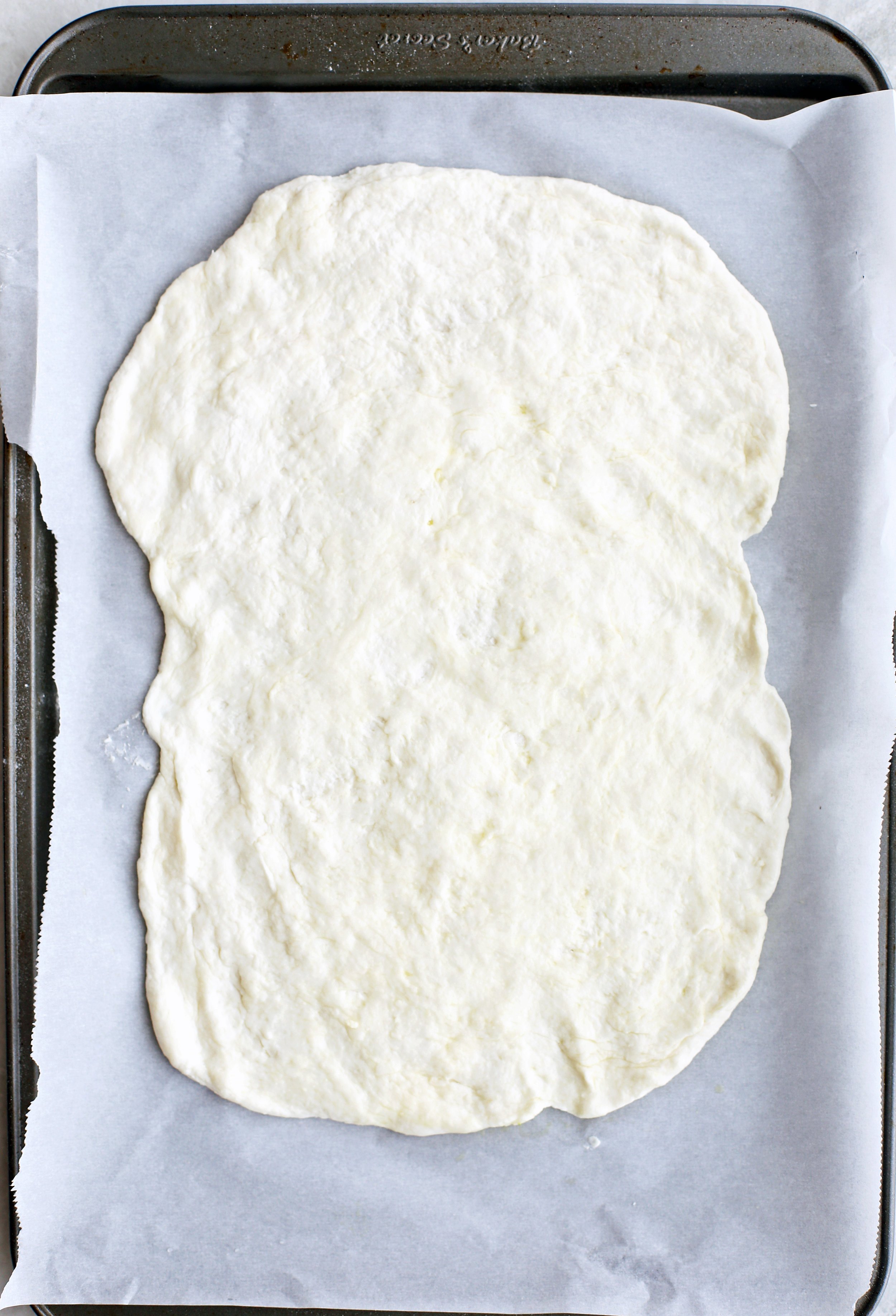 Flatbread dough flattered into a rectangle shape on a parchment-lined baking sheet.