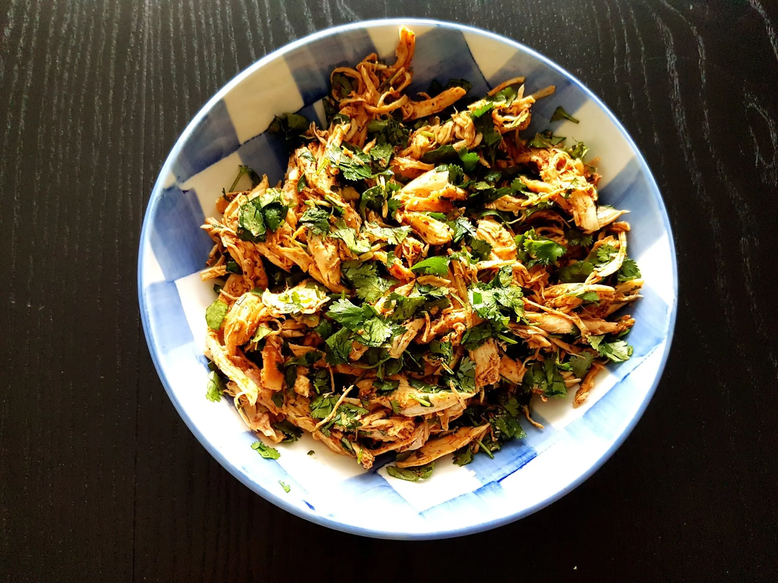 Shredded chicken in a bowl mixed with fresh chopped cilantro.