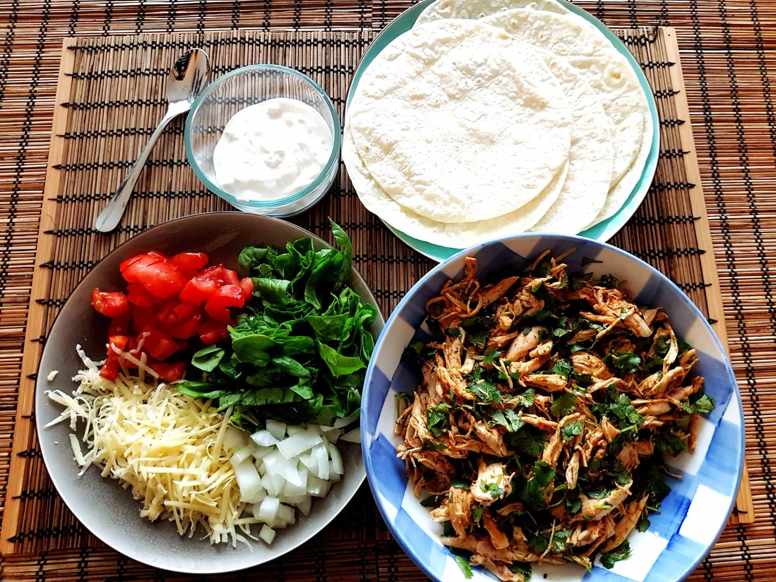 A build-your-own taco station featuring chicken, onions, cheese, tomatoes, spinach, and sour cream.