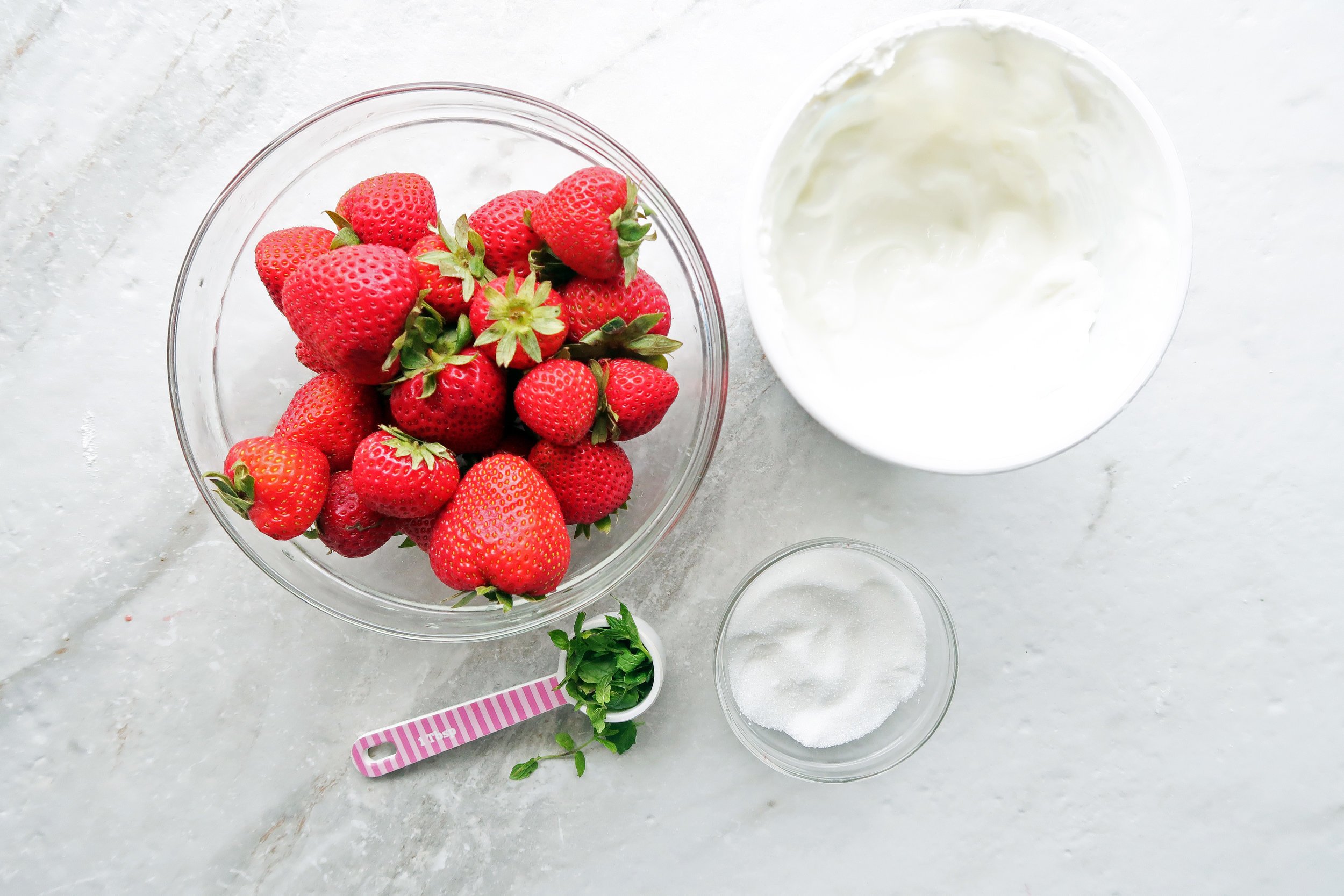 Bowls of juicy strawberries surrounded by tangy mint, and creamy Greek yogurt.