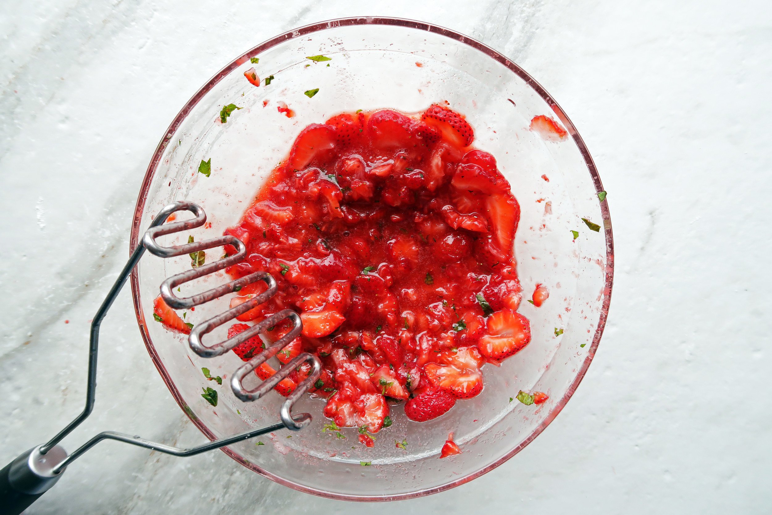 A vibrant bowl of mashed strawberries with pieces of fresh mint.