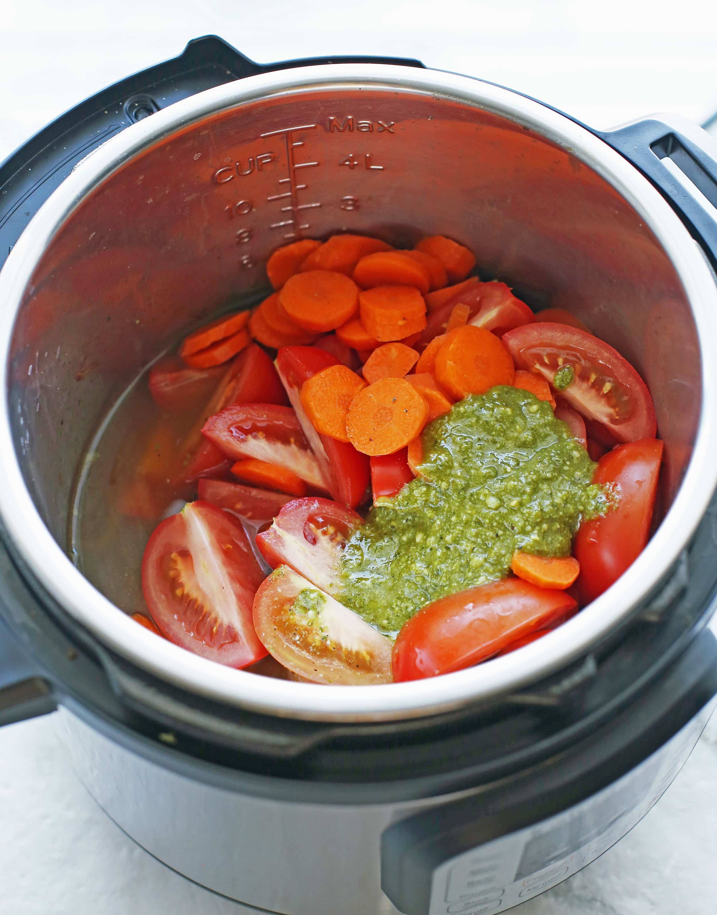 Onions, tomatoes, pesto, carrots, broth, and seasoning in the Instant Pot.
