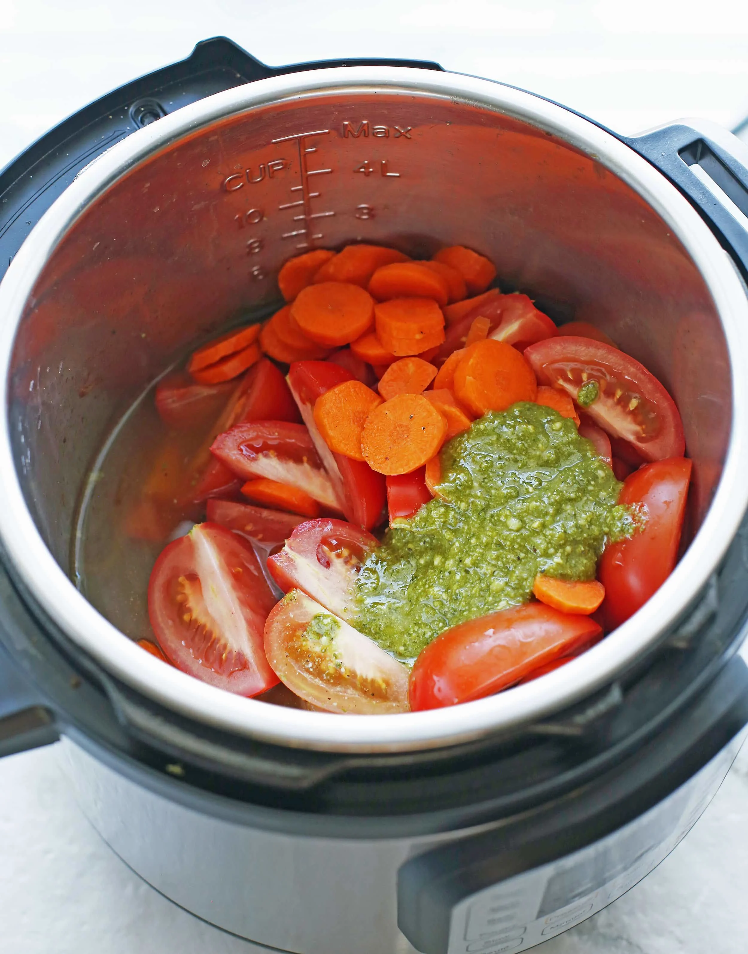 Onions, tomatoes, pesto, carrots, broth, and seasoning in the Instant Pot.