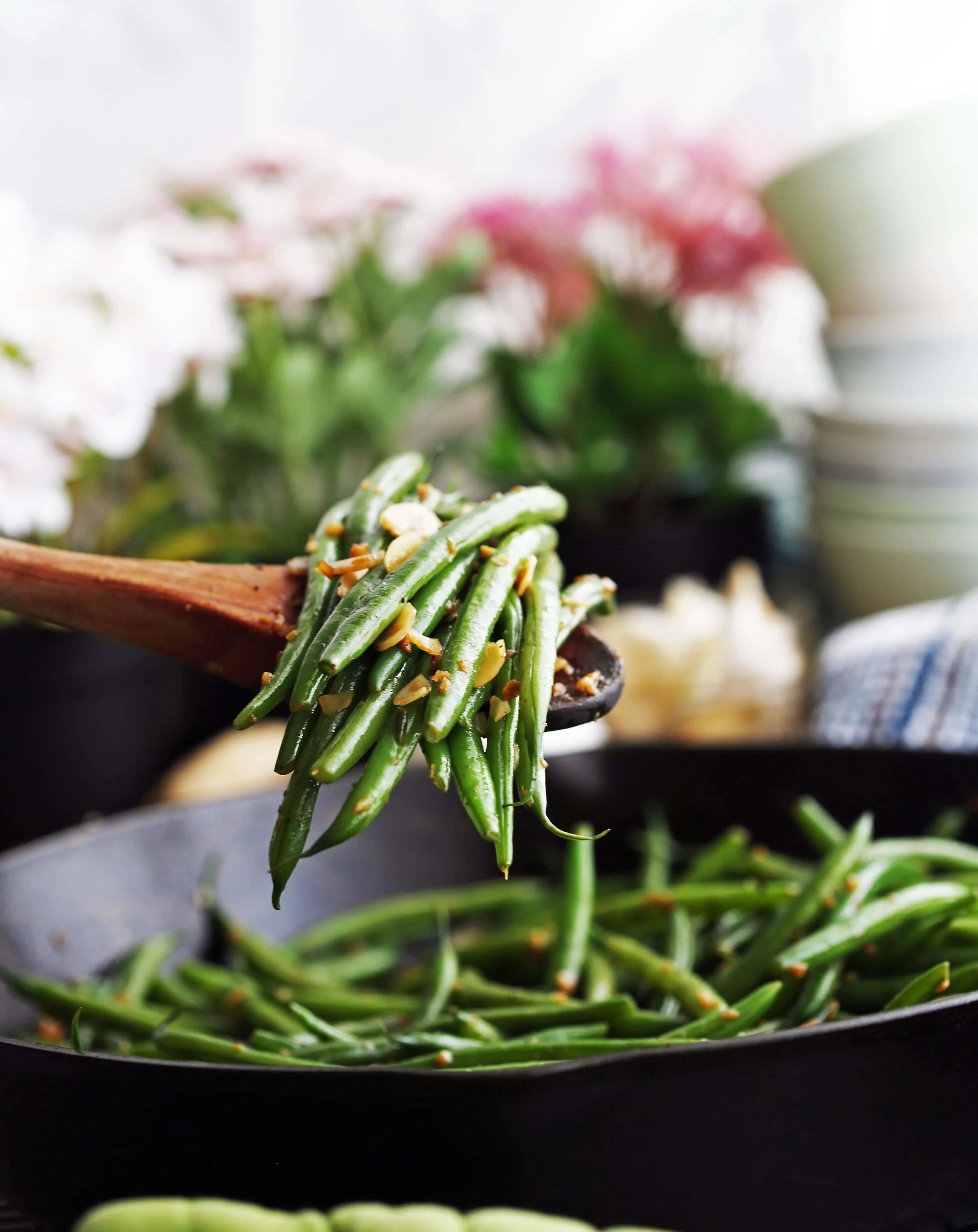 A large wooden spoon holding garlic ginger green beans with more green beans in a skillet in the background.