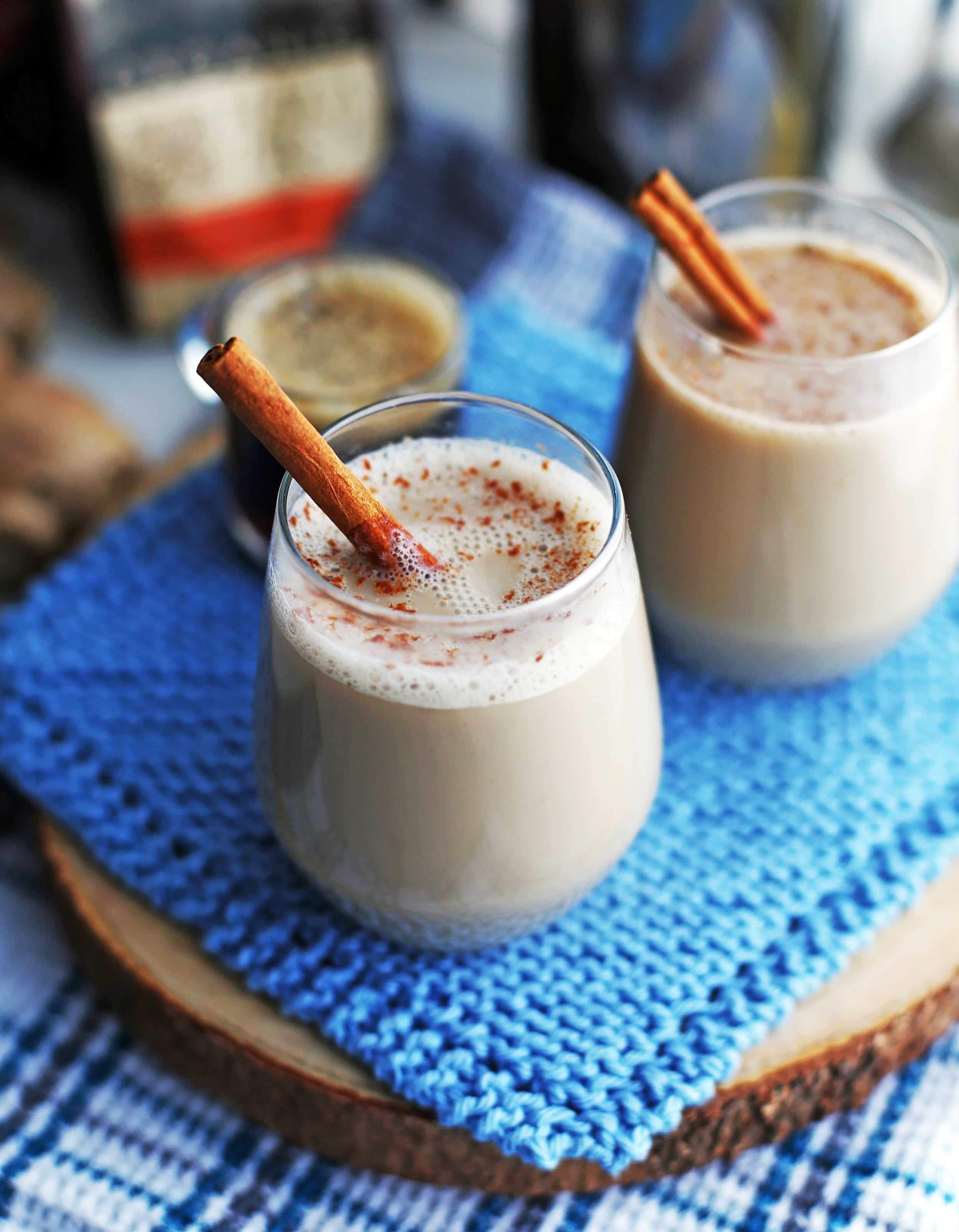 Side view of two honey ginger cinnamon lattes in glass mugs, each with a cinnamon stick as garnish.