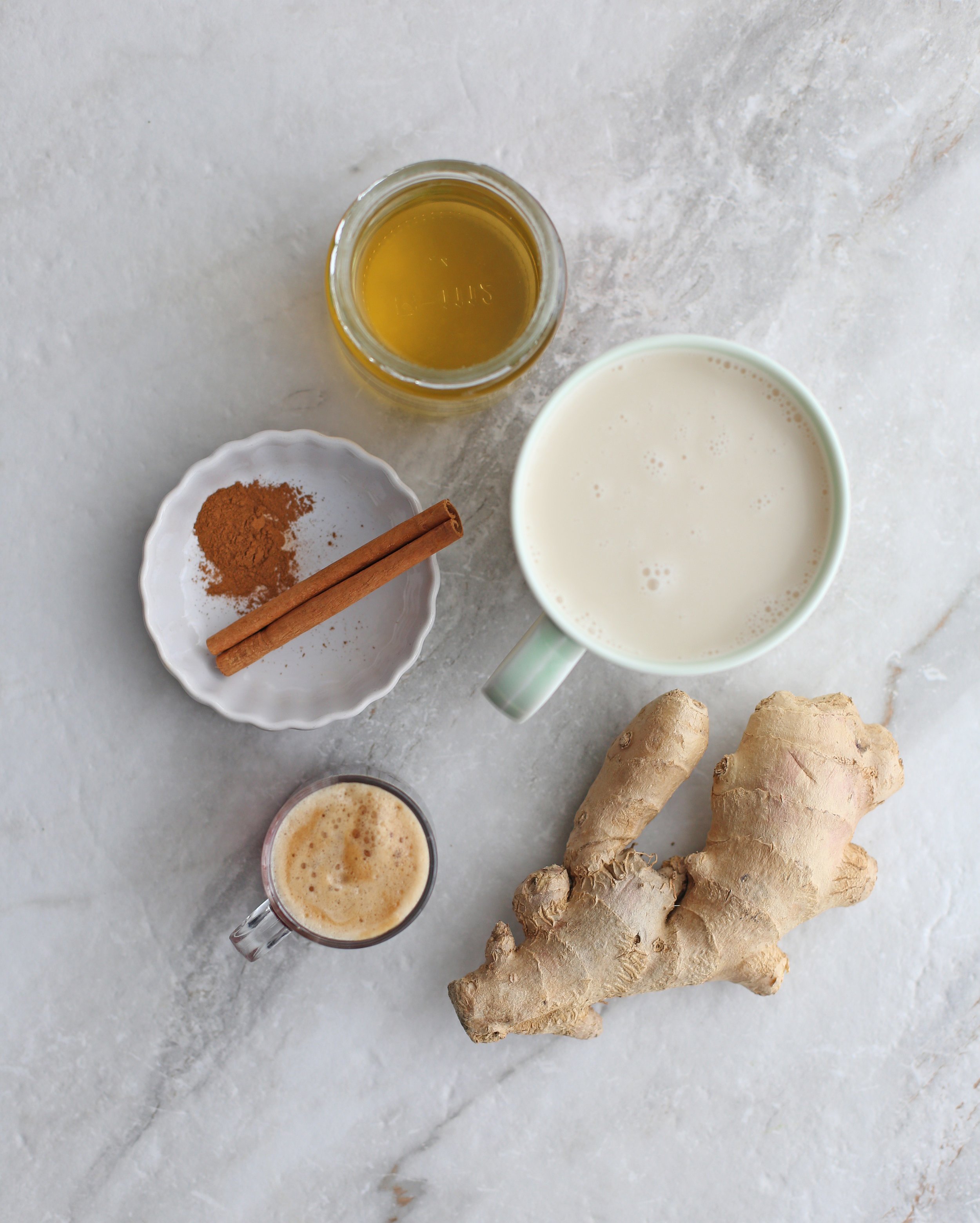 Overhead view of fresh ginger, honey, cinnamon stick, almond milk, and an espresso.