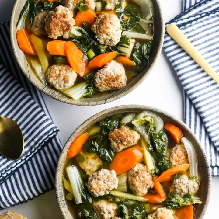 Overhead view of two wooden bowls filled with ginger pork meatball soup with bok choy and carrots.