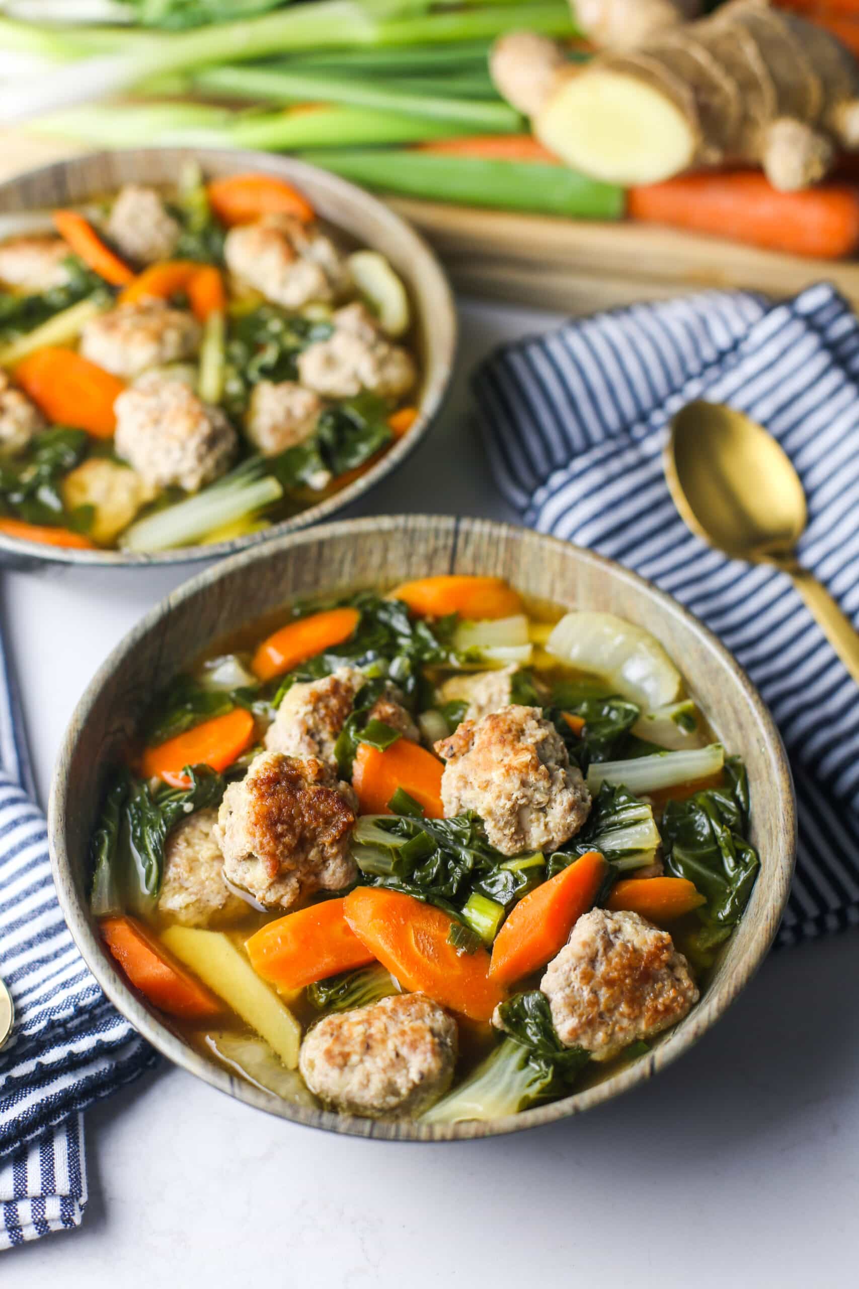 A top angled view of ginger pork meatball soup with bok choy with another bowl of soup in the background.