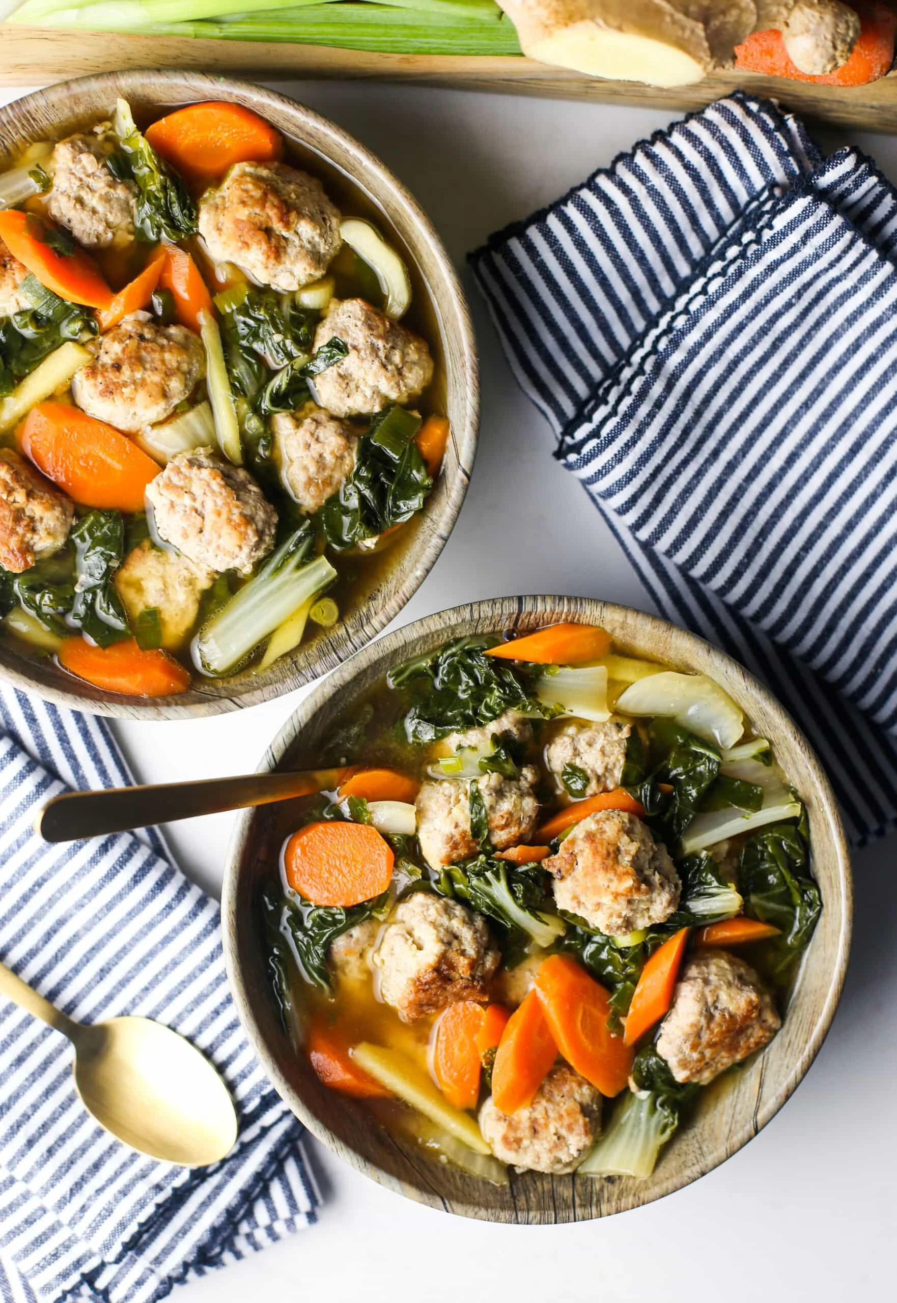 Overhead view of two wooden bowls full of ginger pork meatball soup with bok choy.