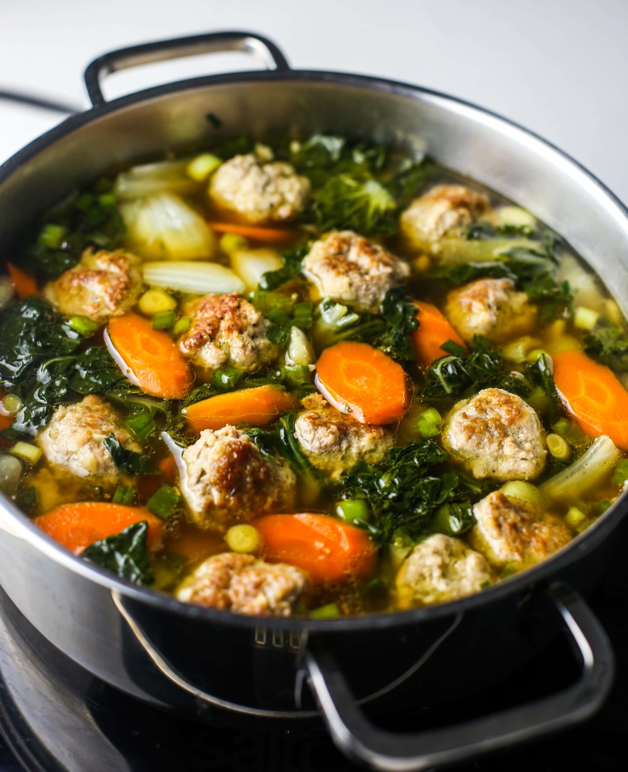 A side angled view of ginger pork meatball with bok choy in a large stainless steel pot.