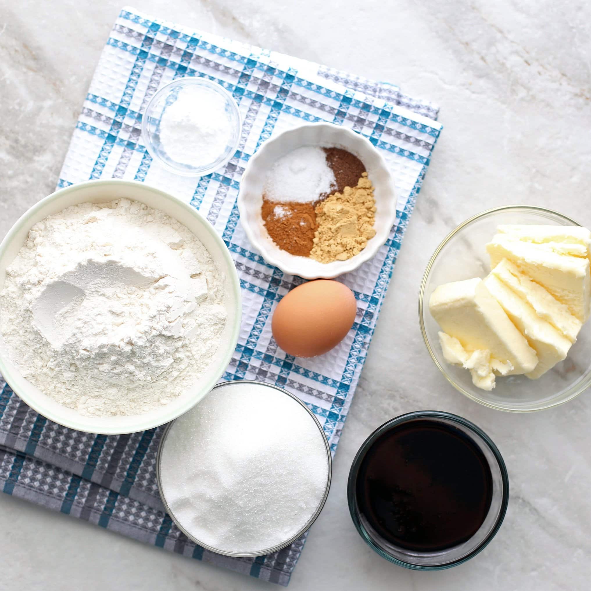 Overhead view of a flour mixture,sugar, egg, molasses, butter, baking soda, and spices.