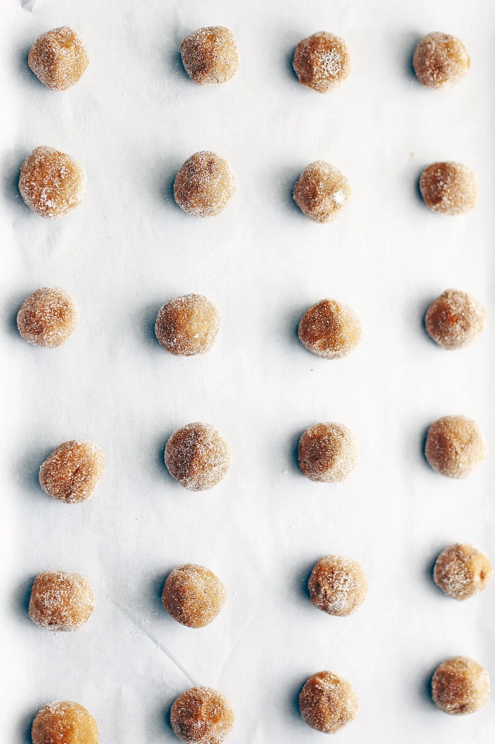 Tablespoon balls of gingersnap cookie dough rolled in sugar on a parchment lined baking sheet.