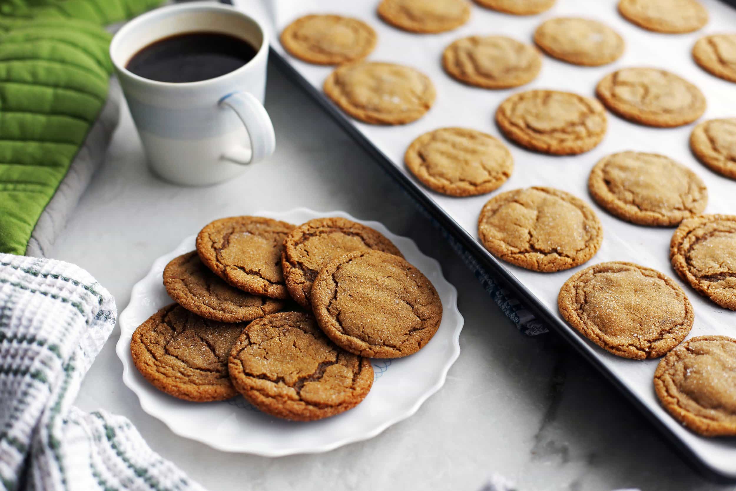 A plate full of chewy gingersnap (ginger molasses) cookies with more cookies on a baking sheet beside it.