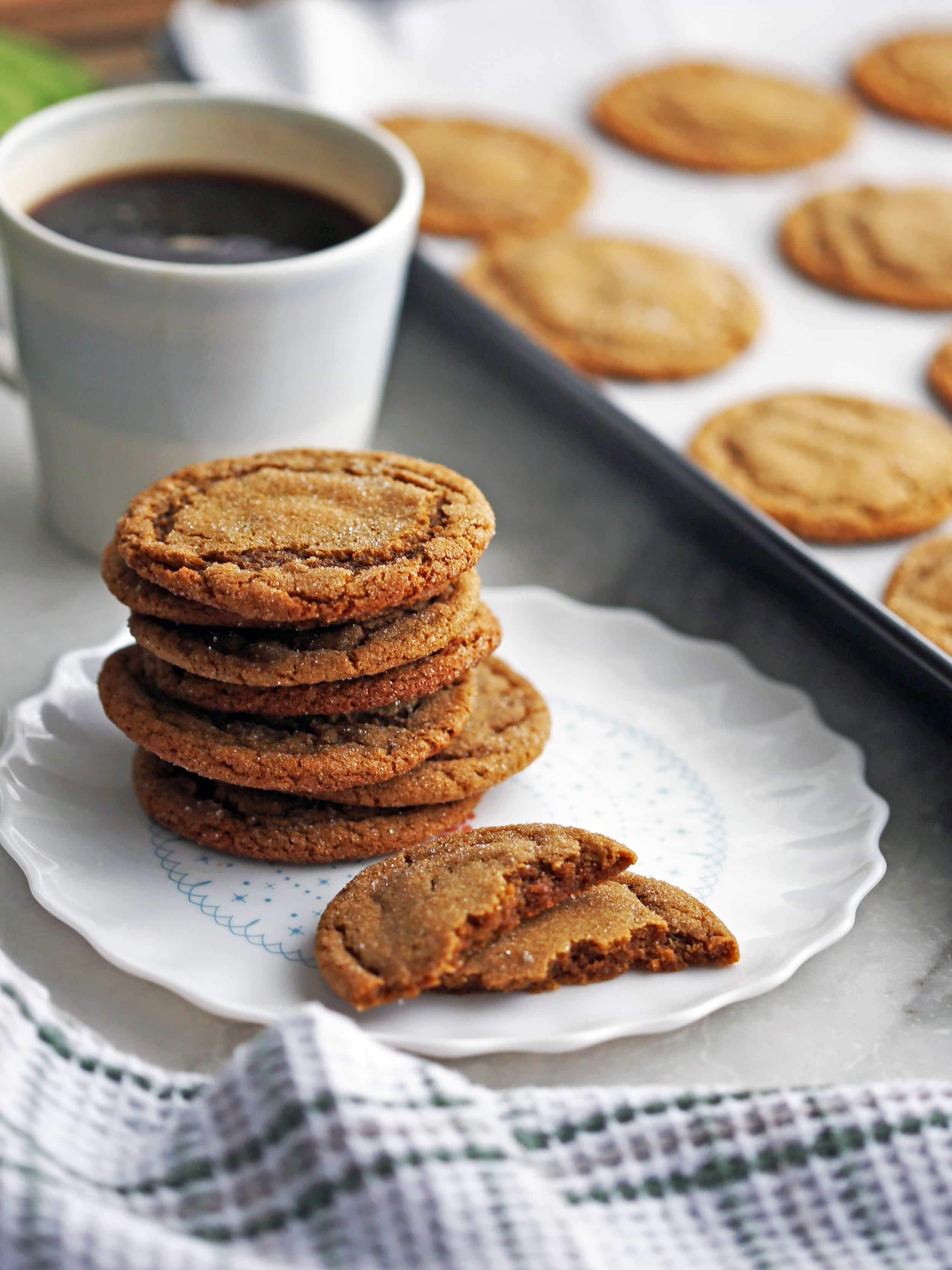 A closeup side view of a stack of chewy gingersnap (ginger molasses) cookies with coffee and more cookies in the background.
