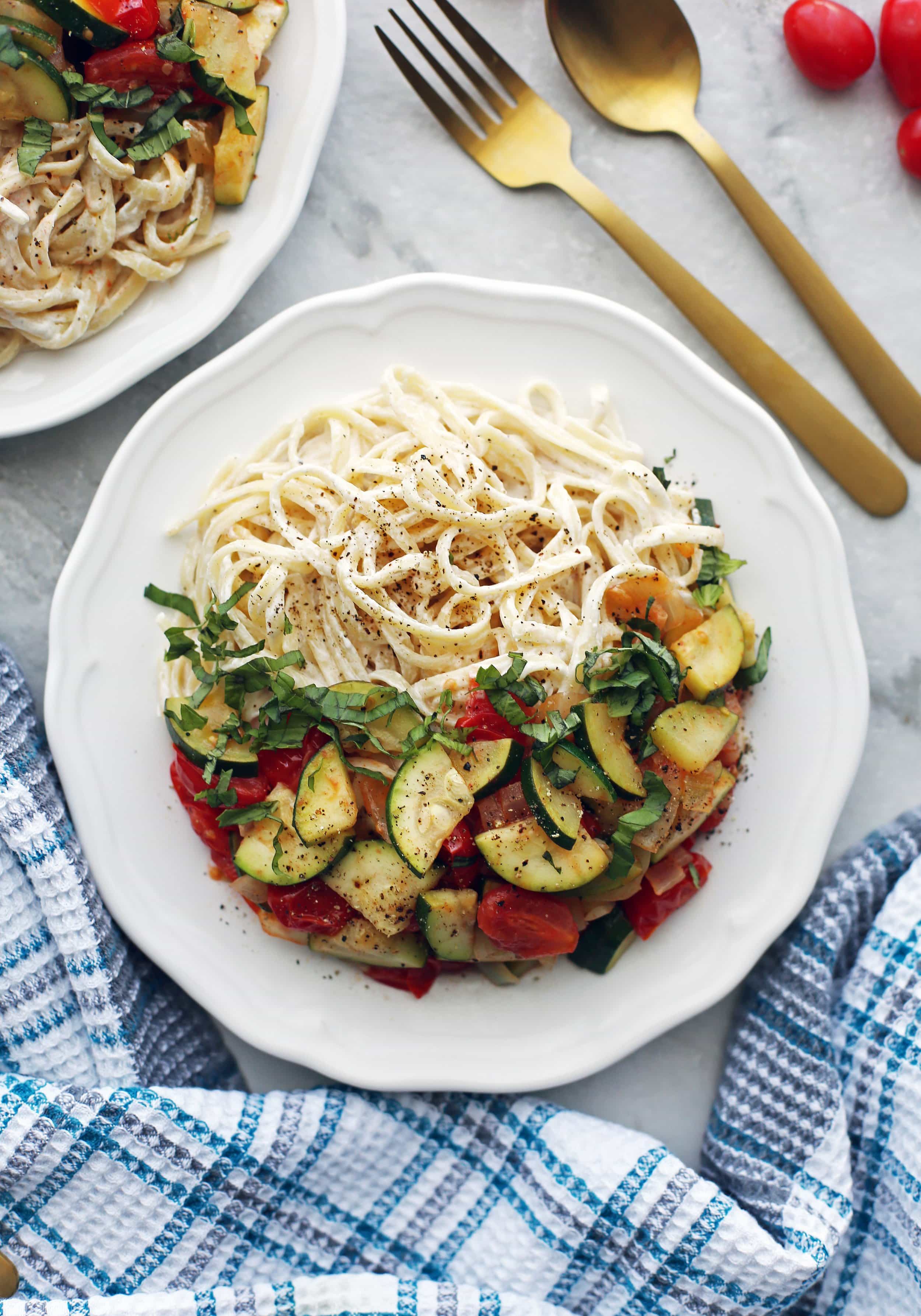 Overhead view of a white plate full of creamy goat cheese pasta with zucchini and tomatoes.