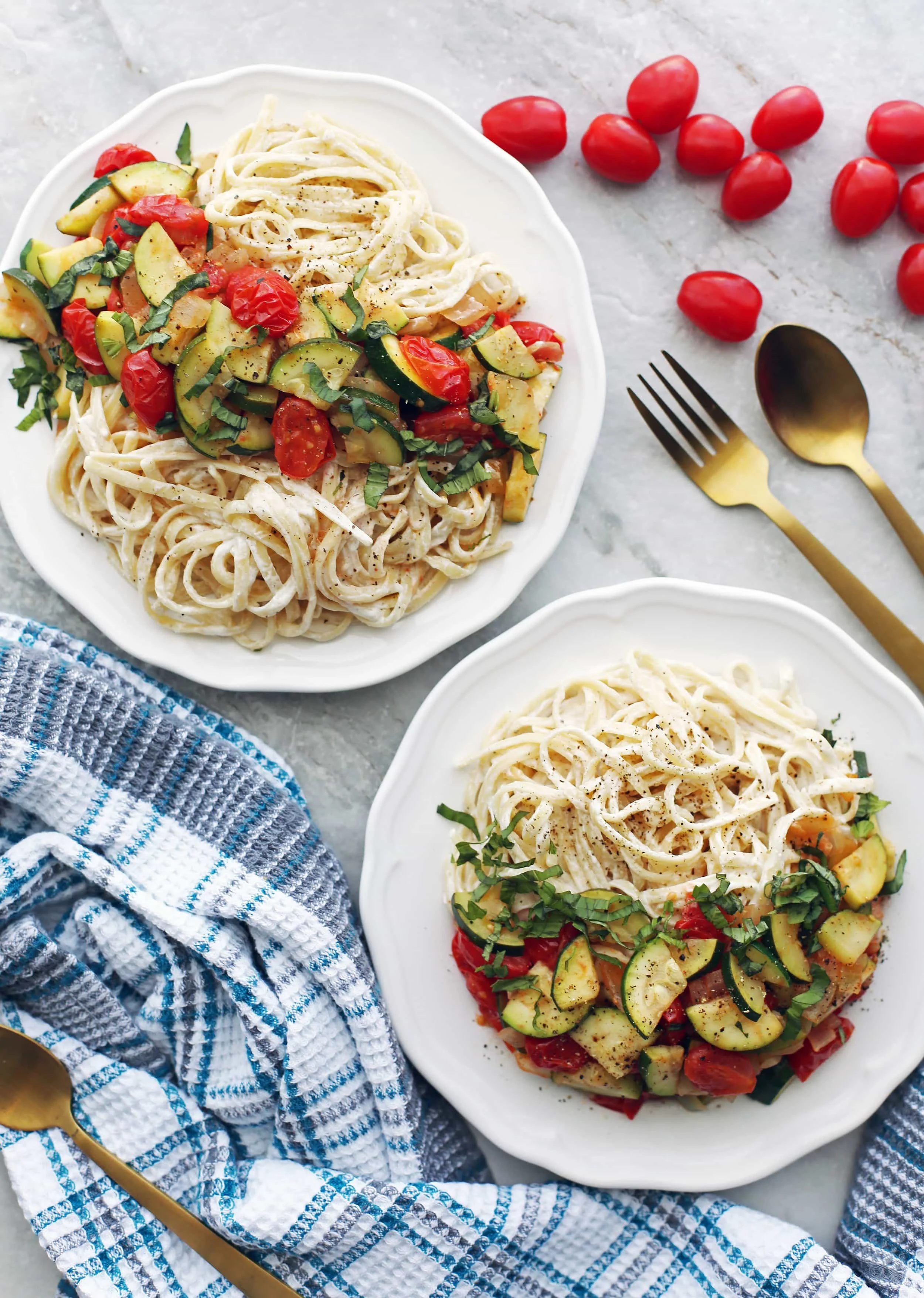Two white plates containing creamy goat cheese pasta with sauteed zucchini and tomatoes and fresh basil.