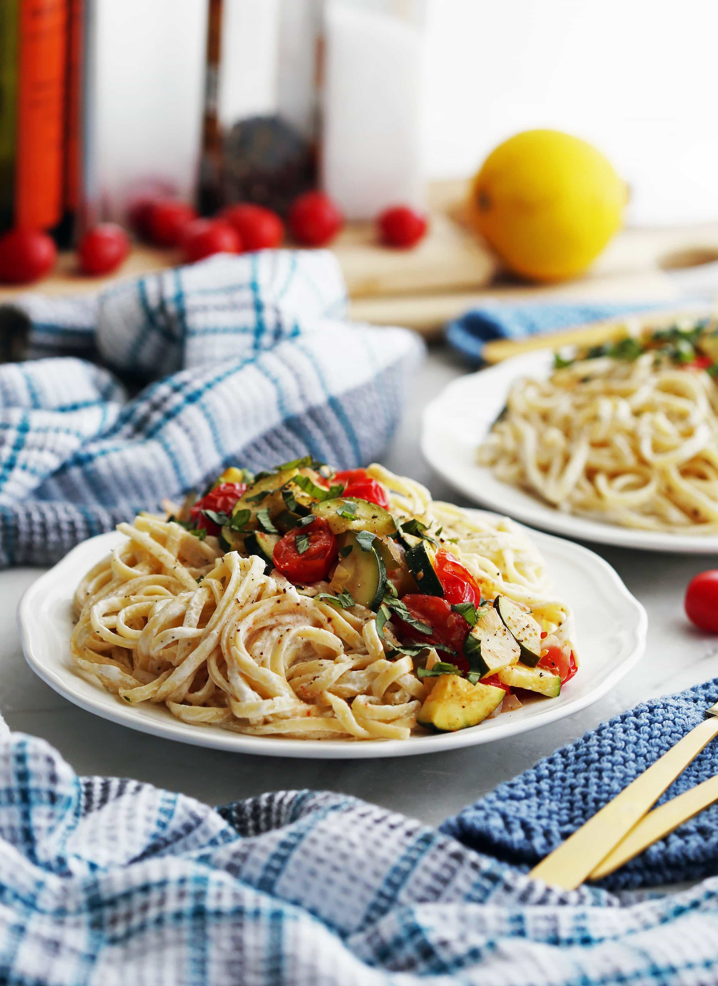 Creamy linguine pasta with goat cheese sauce topped with sautéed tomatoes, zucchini, and fresh basil on a white plate.