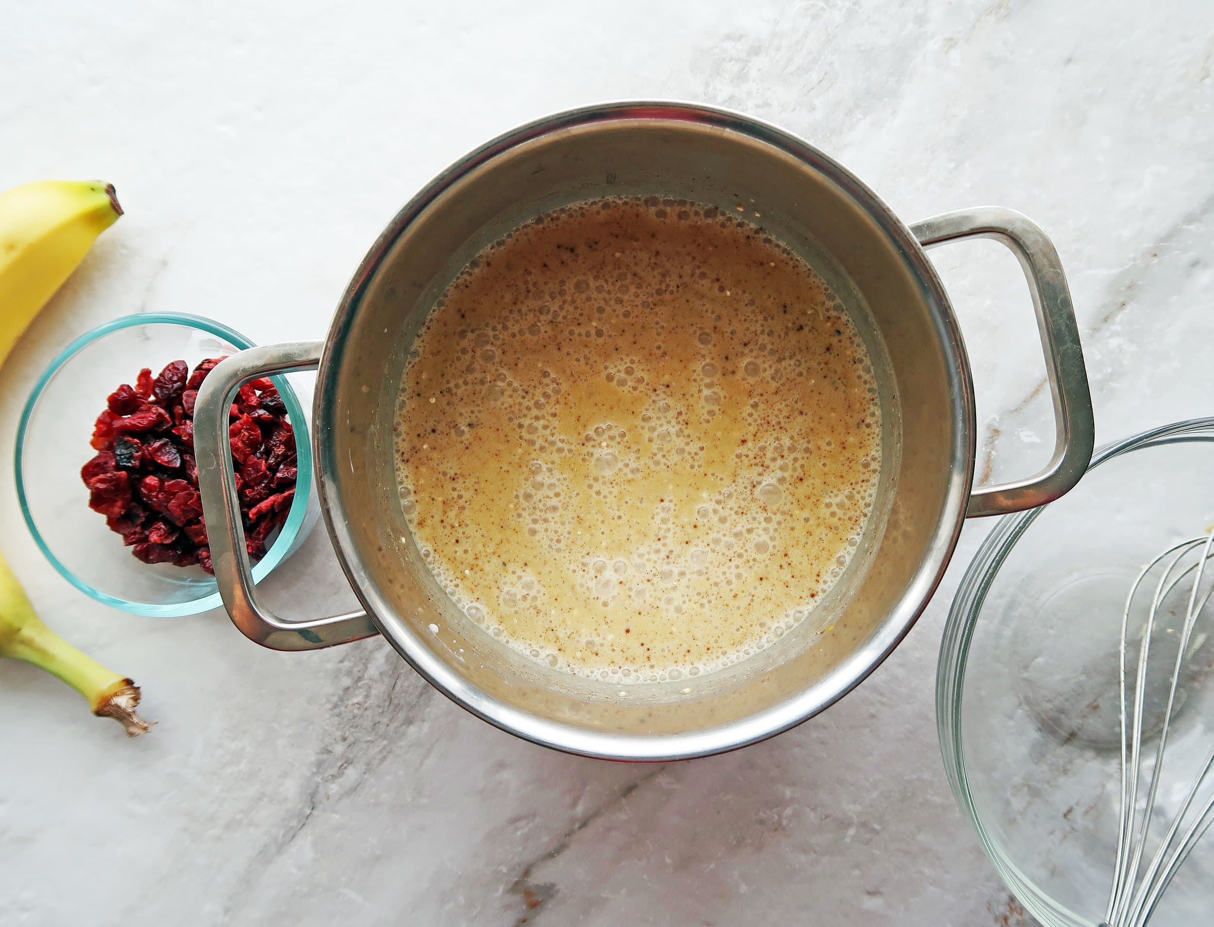 Golden milk ingredients in a small pot; dried cranberries and a banana to its side.