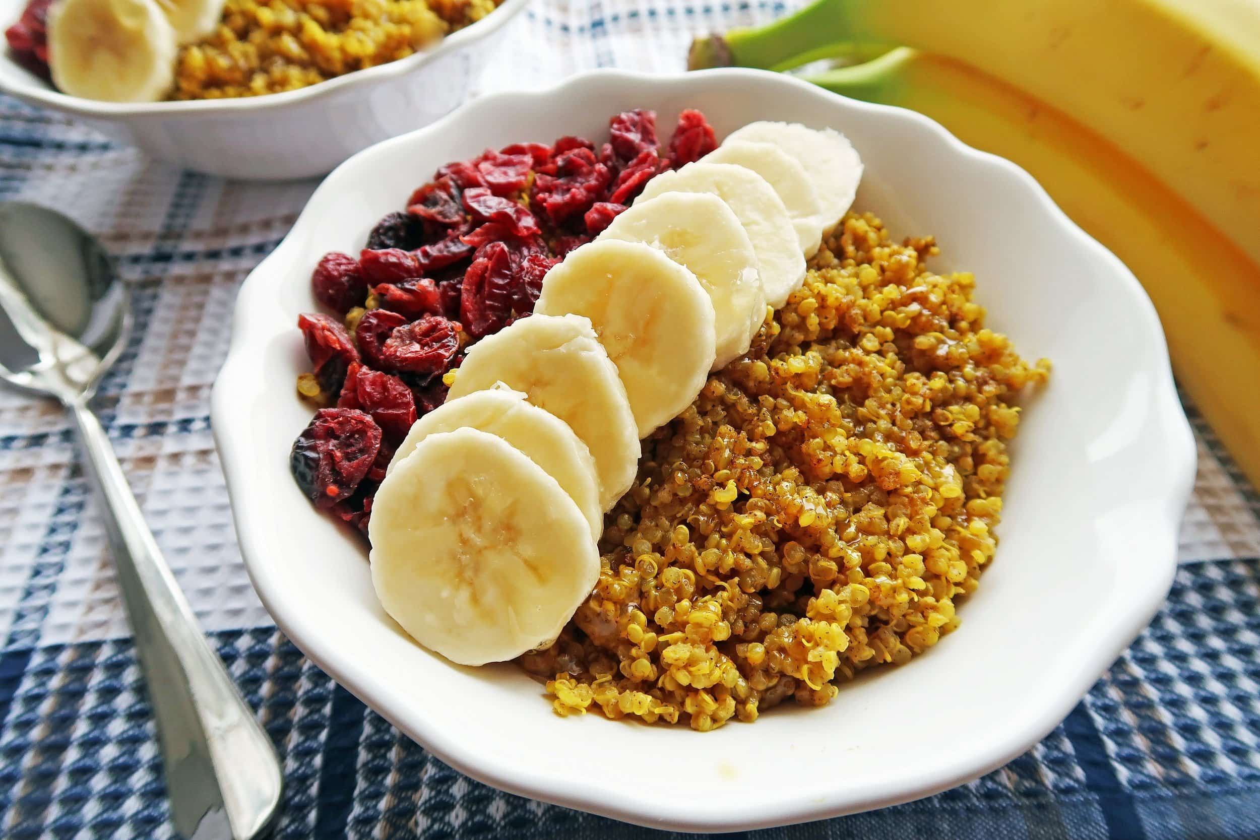 Closeup of golden milk (turmeric latte) quinoa bowl with banana slices and dried cranberries.